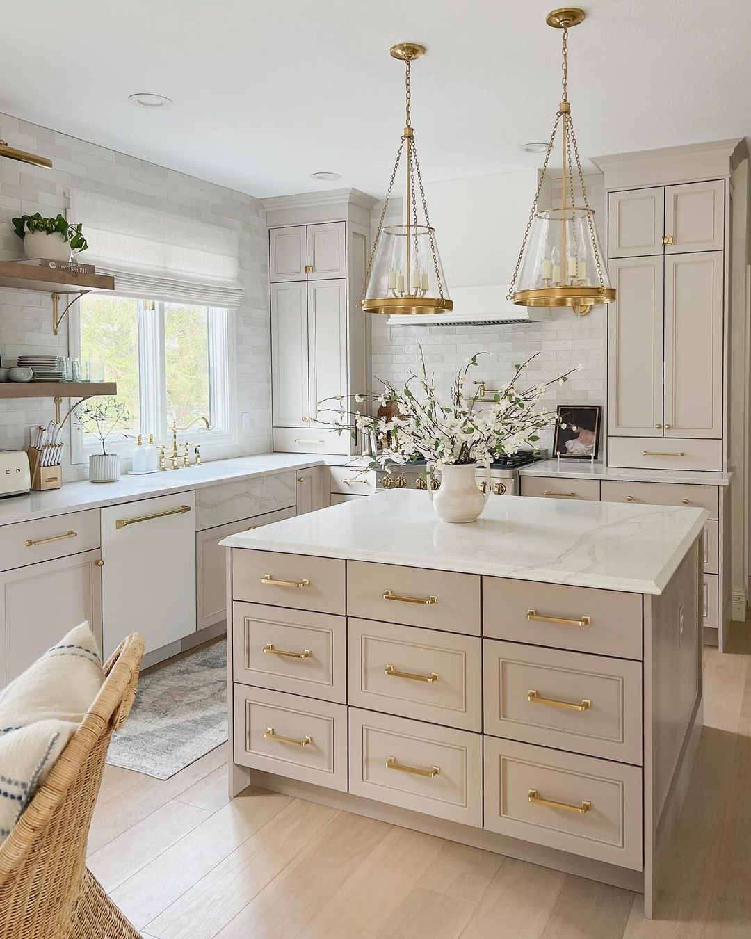 A sophisticated kitchen design featuring taupe cabinetry with gold hardware, marble countertops, and stylish pendant lighting.