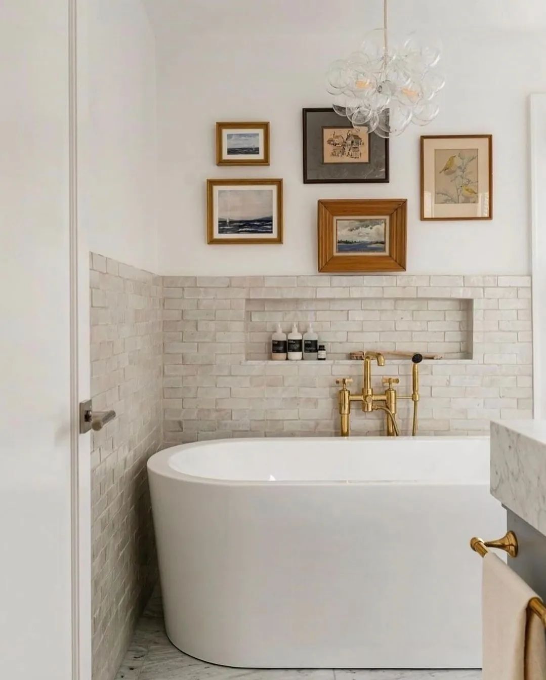 A modern white bathroom featuring a freestanding bathtub with brushed gold fixtures