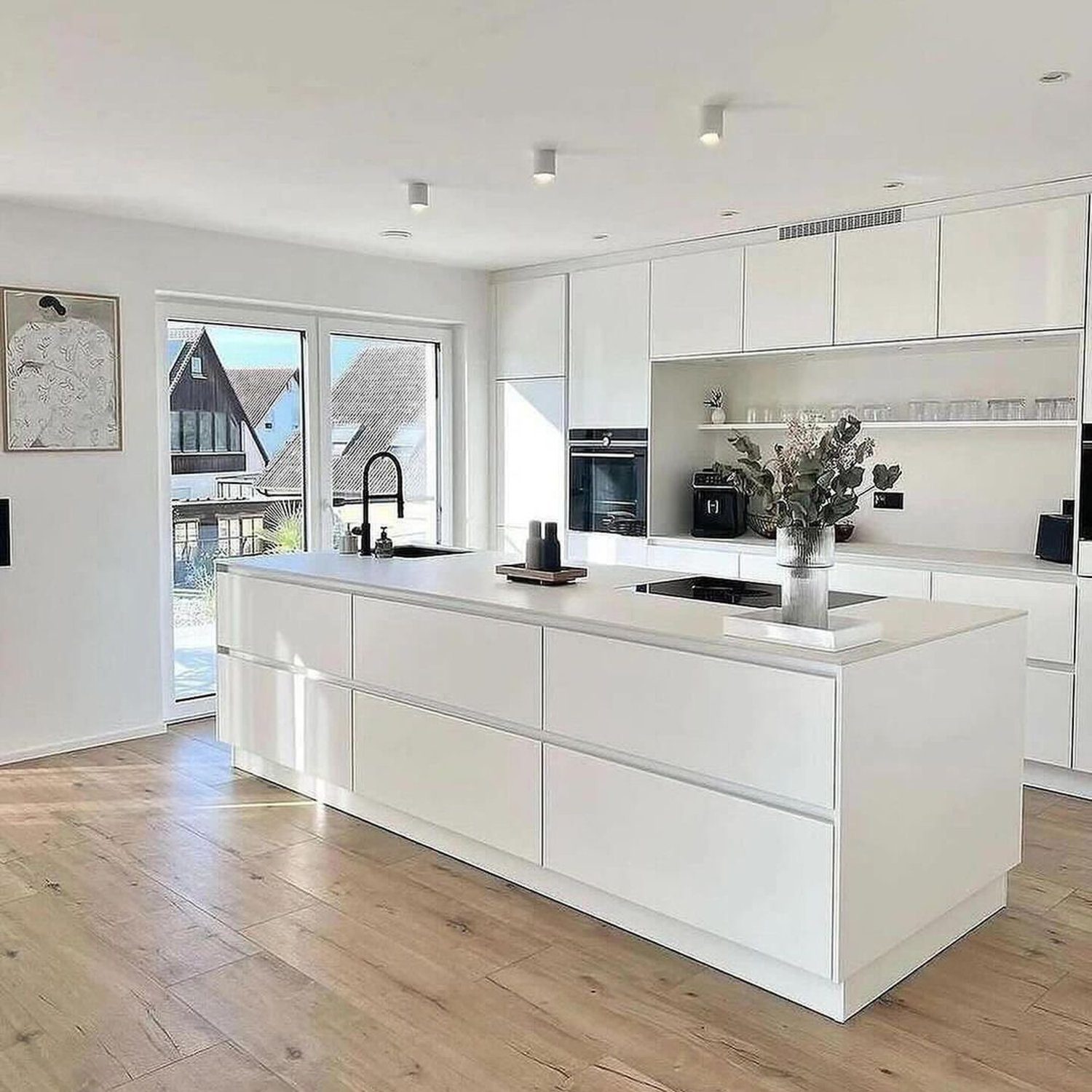 A bright and airy modern kitchen with minimalist white cabinetry and hardwood flooring.