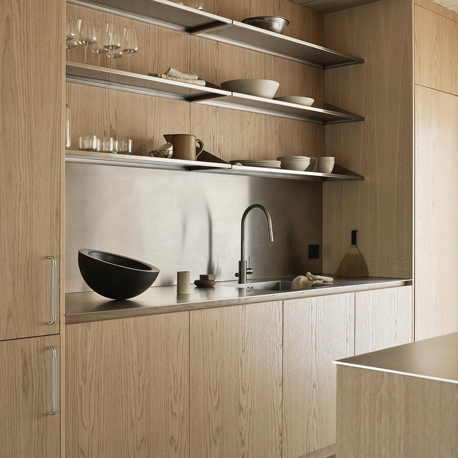 A modern kitchen with seamless wood cabinetry and open shelving, featuring a stainless steel backsplash and minimalist decor.