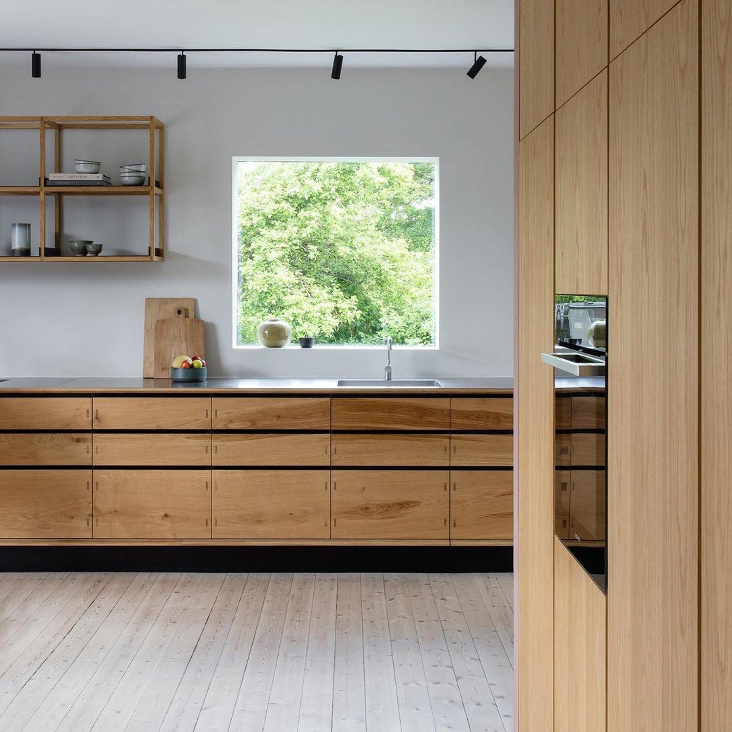 A modern kitchen with floor-to-ceiling wooden cabinetry and a large window overlooking green foliage.