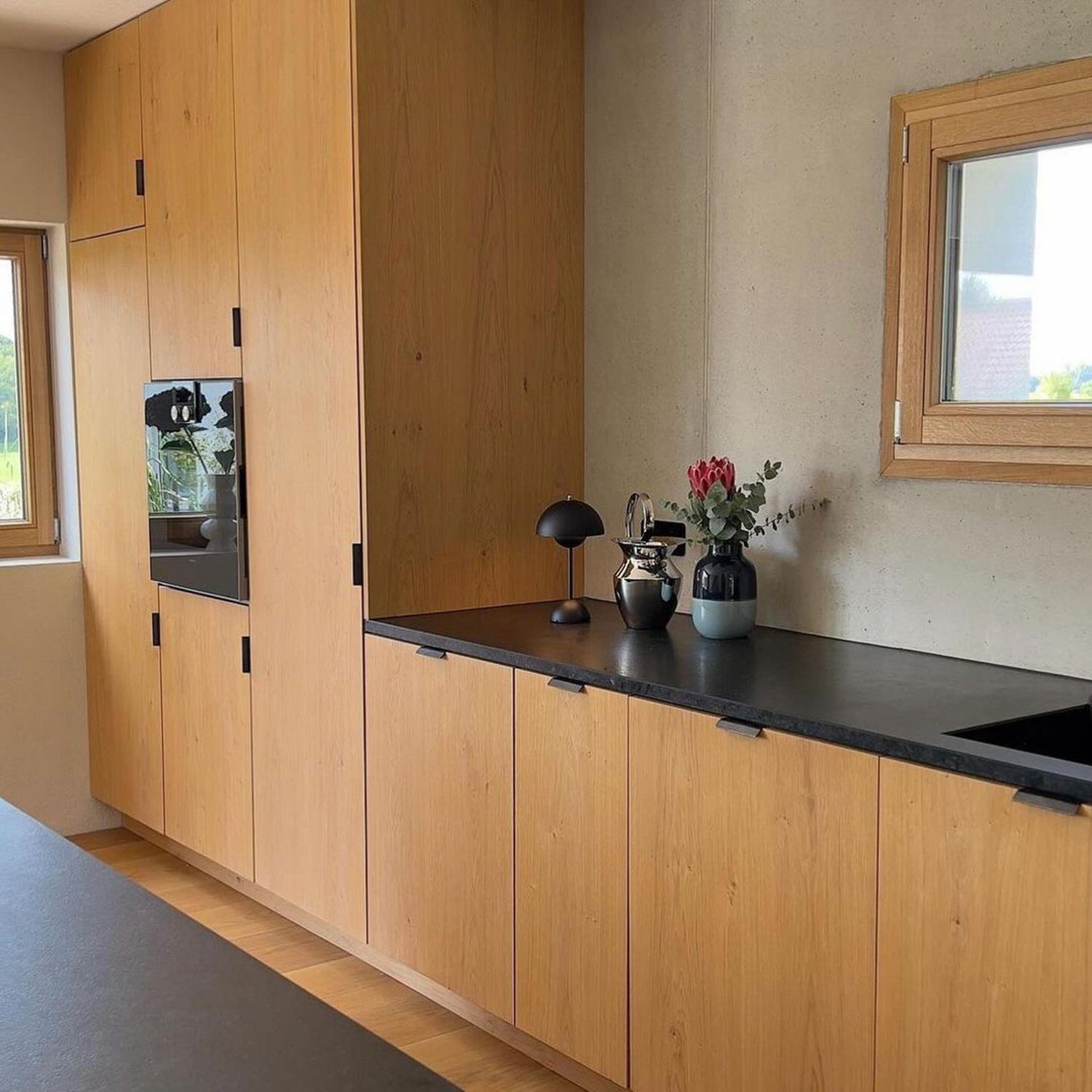 A modern kitchen space featuring warm wooden cabinetry and sleek black countertops