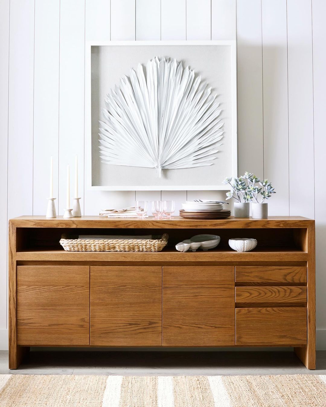 A chic wooden sideboard against a white paneled wall, styled with minimal decor