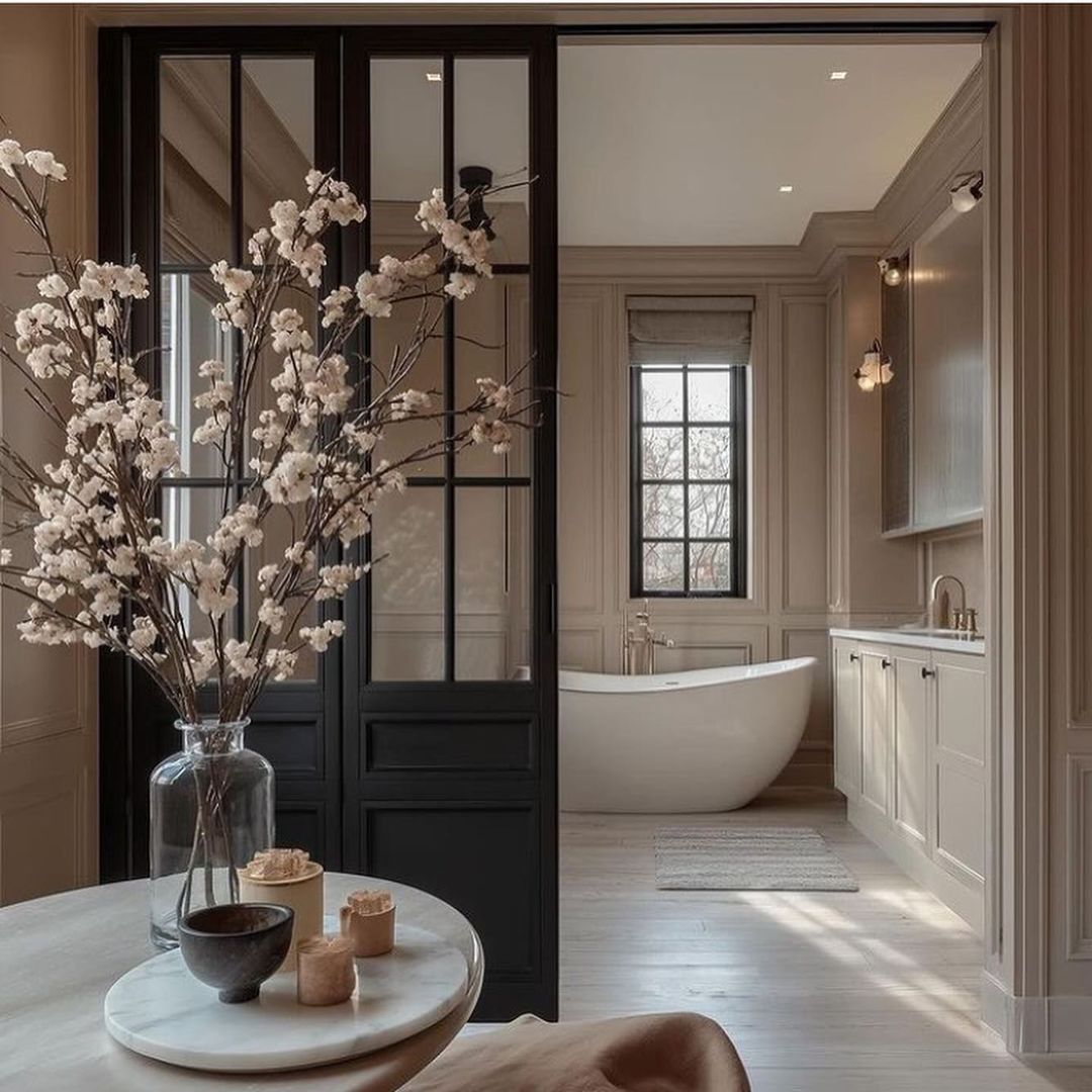 A sophisticated monochromatic bathroom boasting a freestanding tub and black-framed glass doors