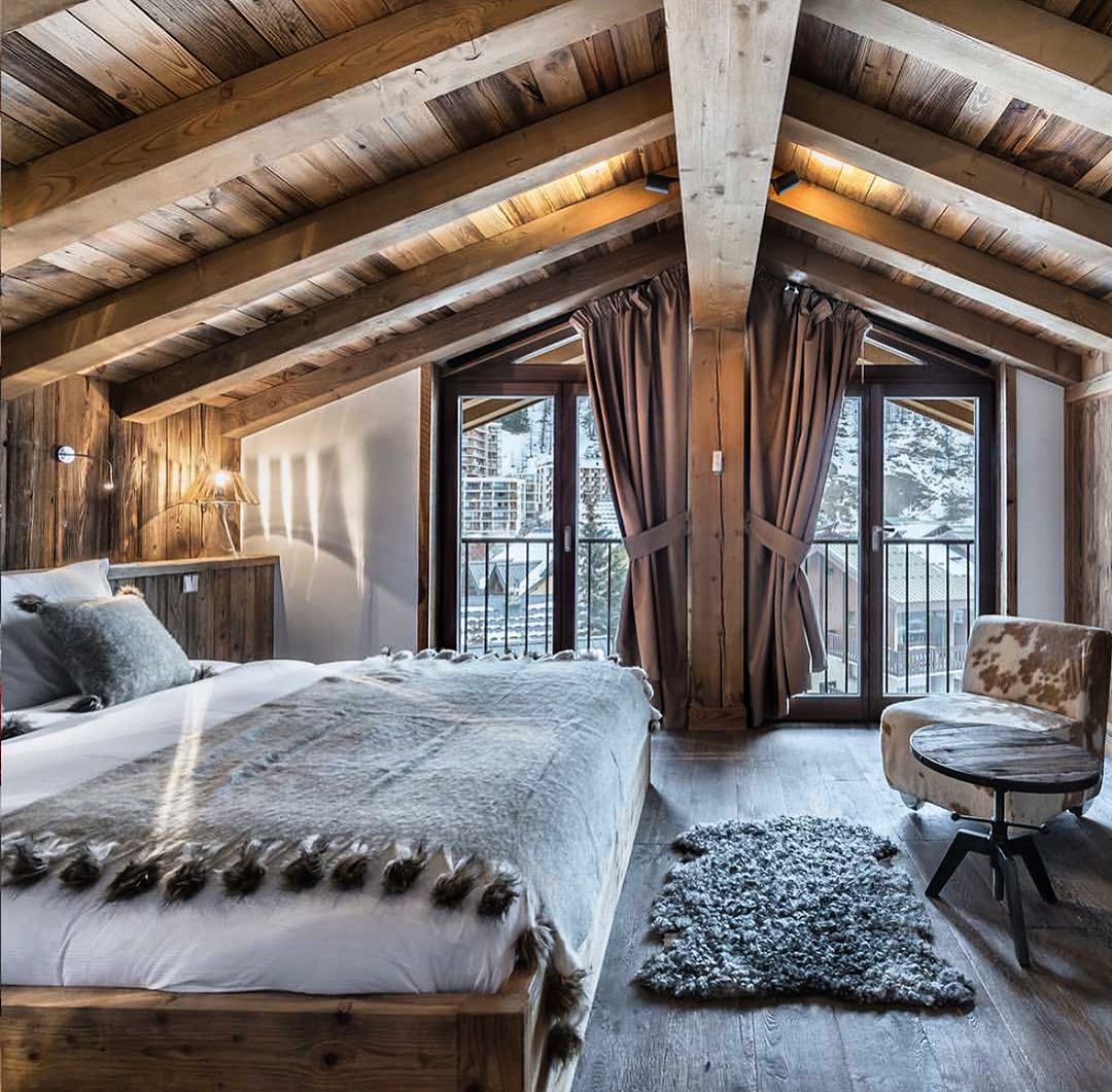 Cozy mountain lodge bedroom with a rustic wood beam ceiling and snowy view