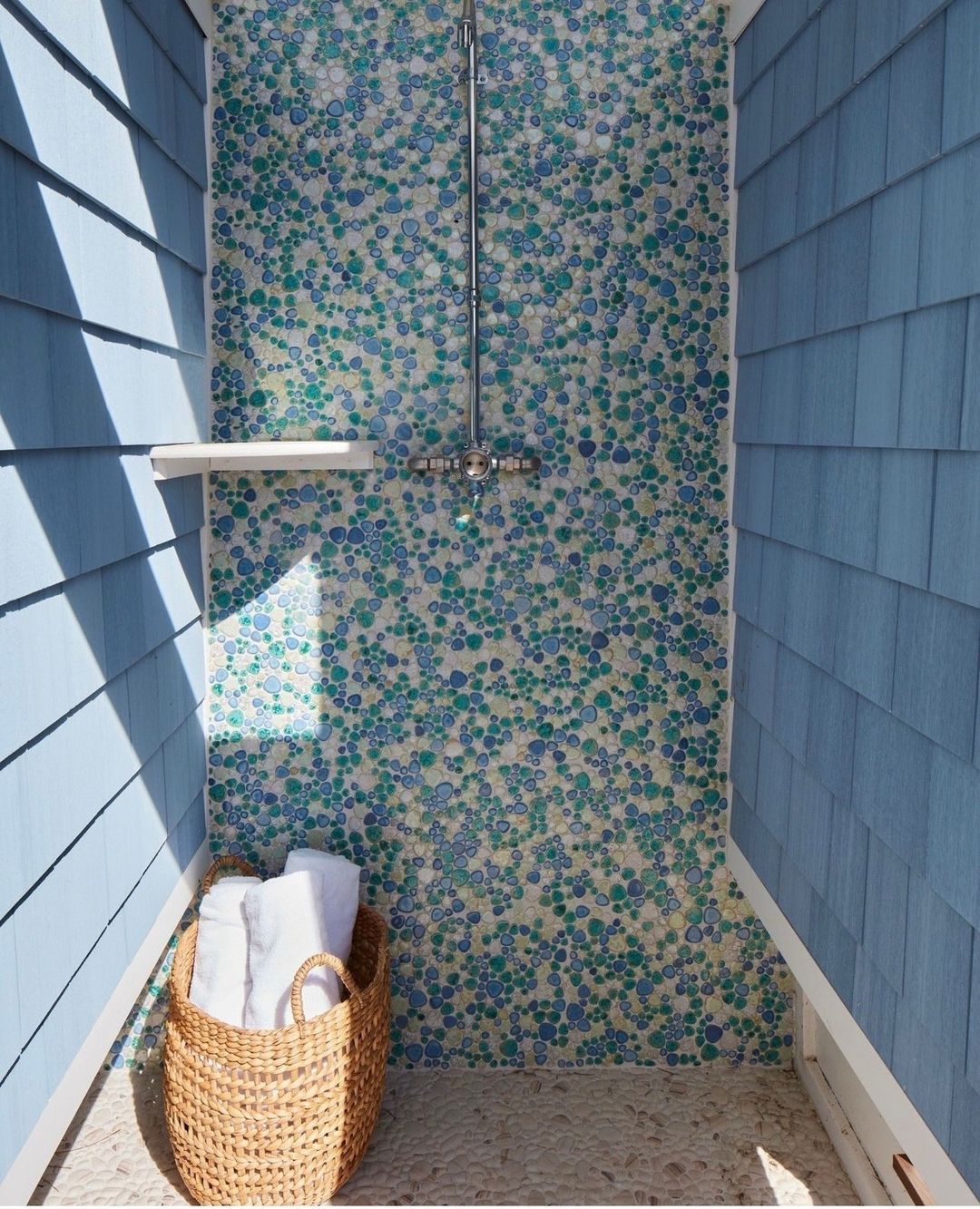 A uniquely tiled outdoor shower with varying shades of blue and green mosaic tiles