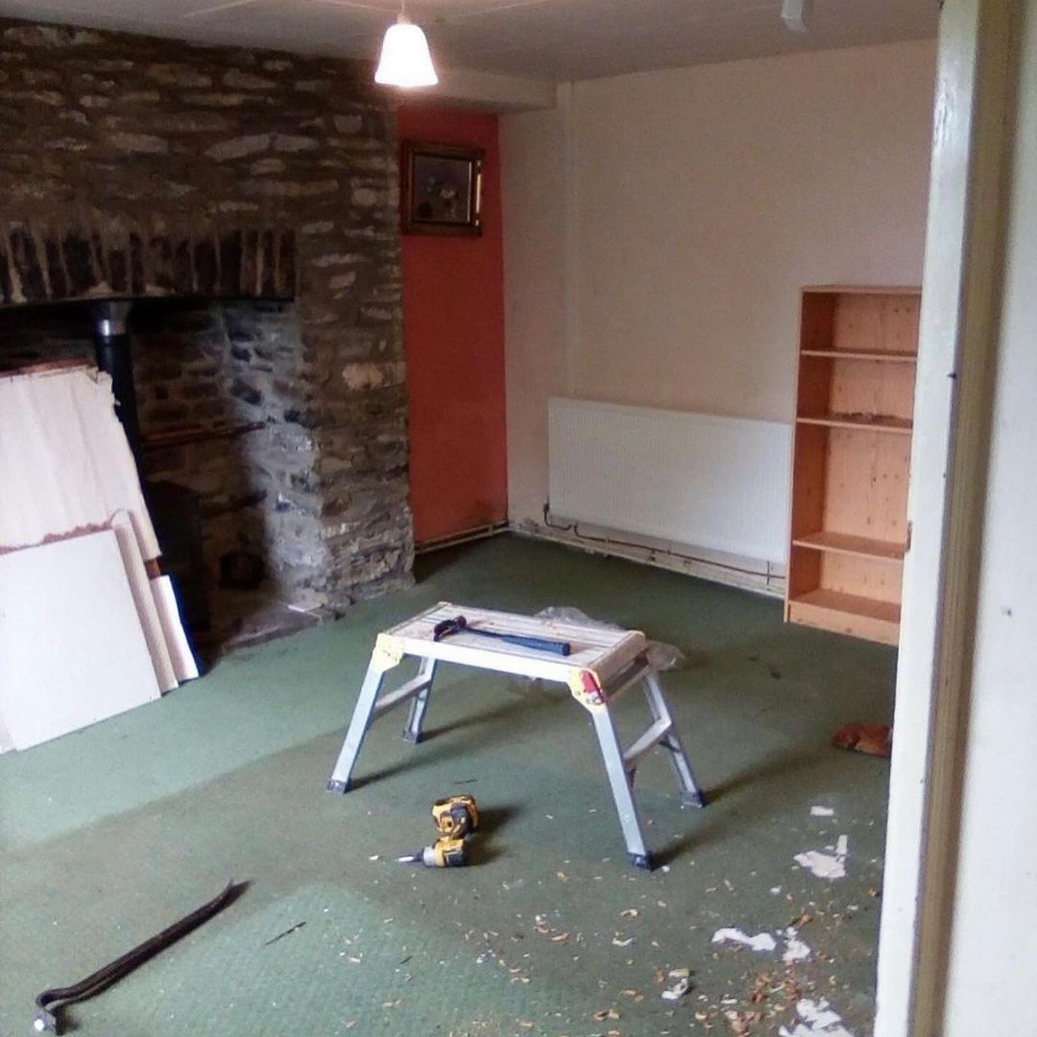 A room undergoing renovations with a stone fireplace and green carpet