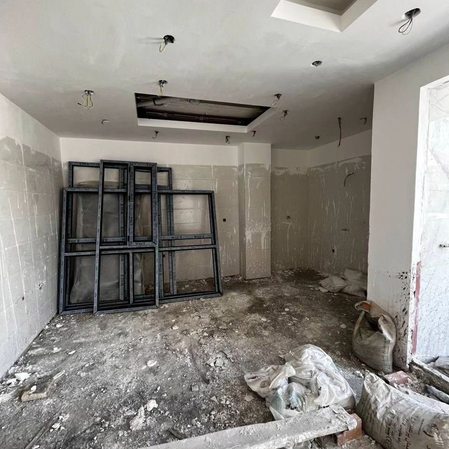 A room under construction with unfinished walls, ceiling details, and windows standing on the floor.