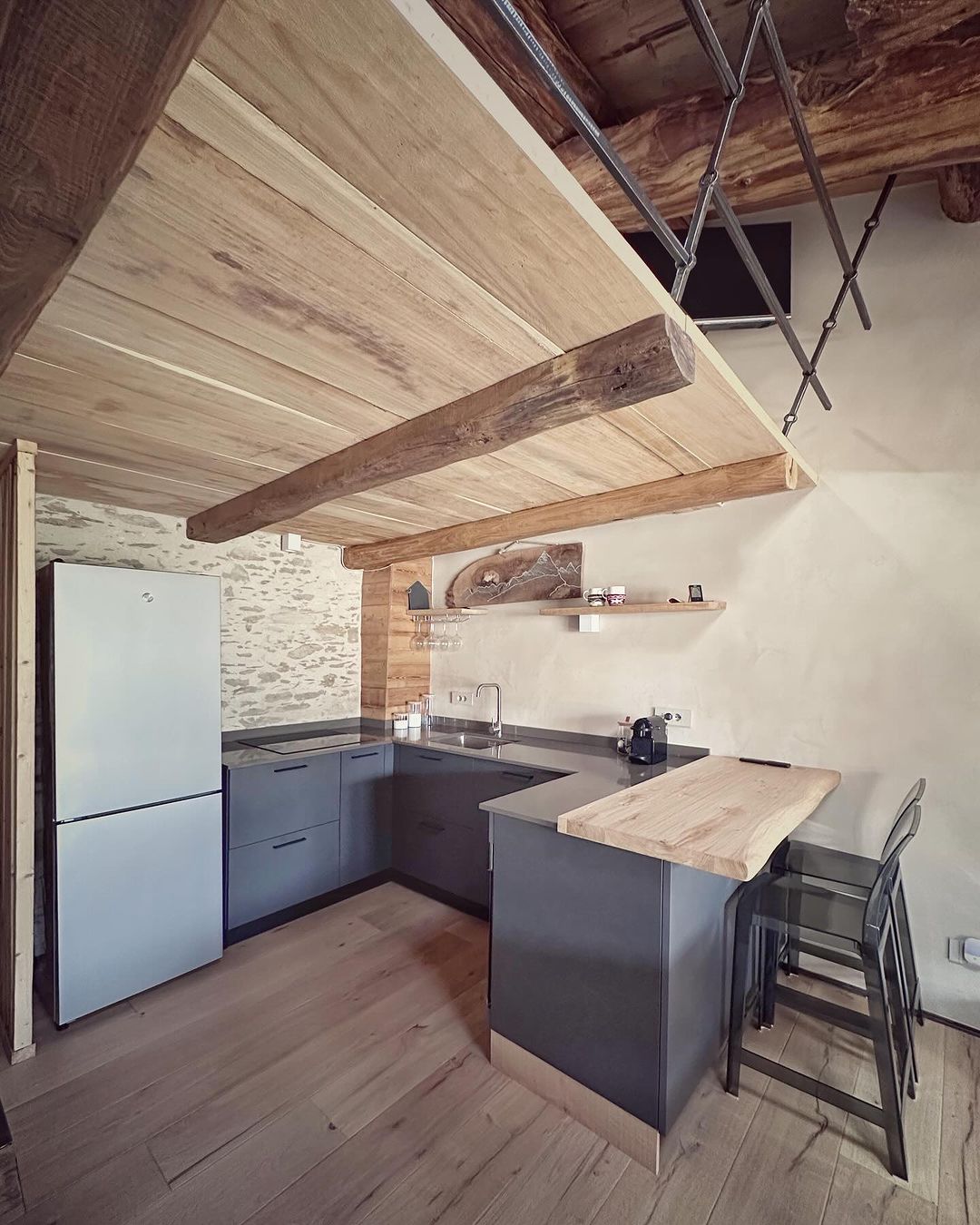 A rustic-modern kitchen design featuring exposed wooden beams, stone walls, and sleek grey cabinetry