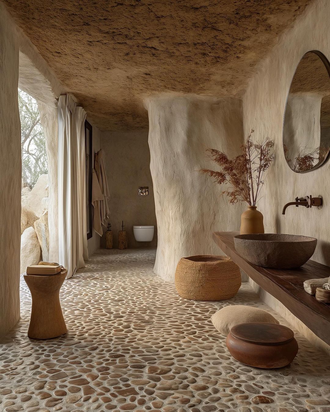 A rustic-inspired bathroom with a pebble floor and plaster walls reflecting a fusion of nature and comfort