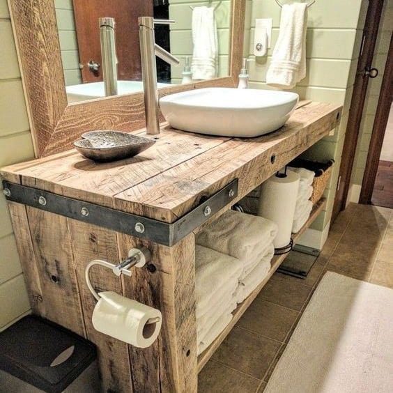 A rustic bathroom vanity crafted from reclaimed wood with metal accents, a white vessel sink, and a towel shelf