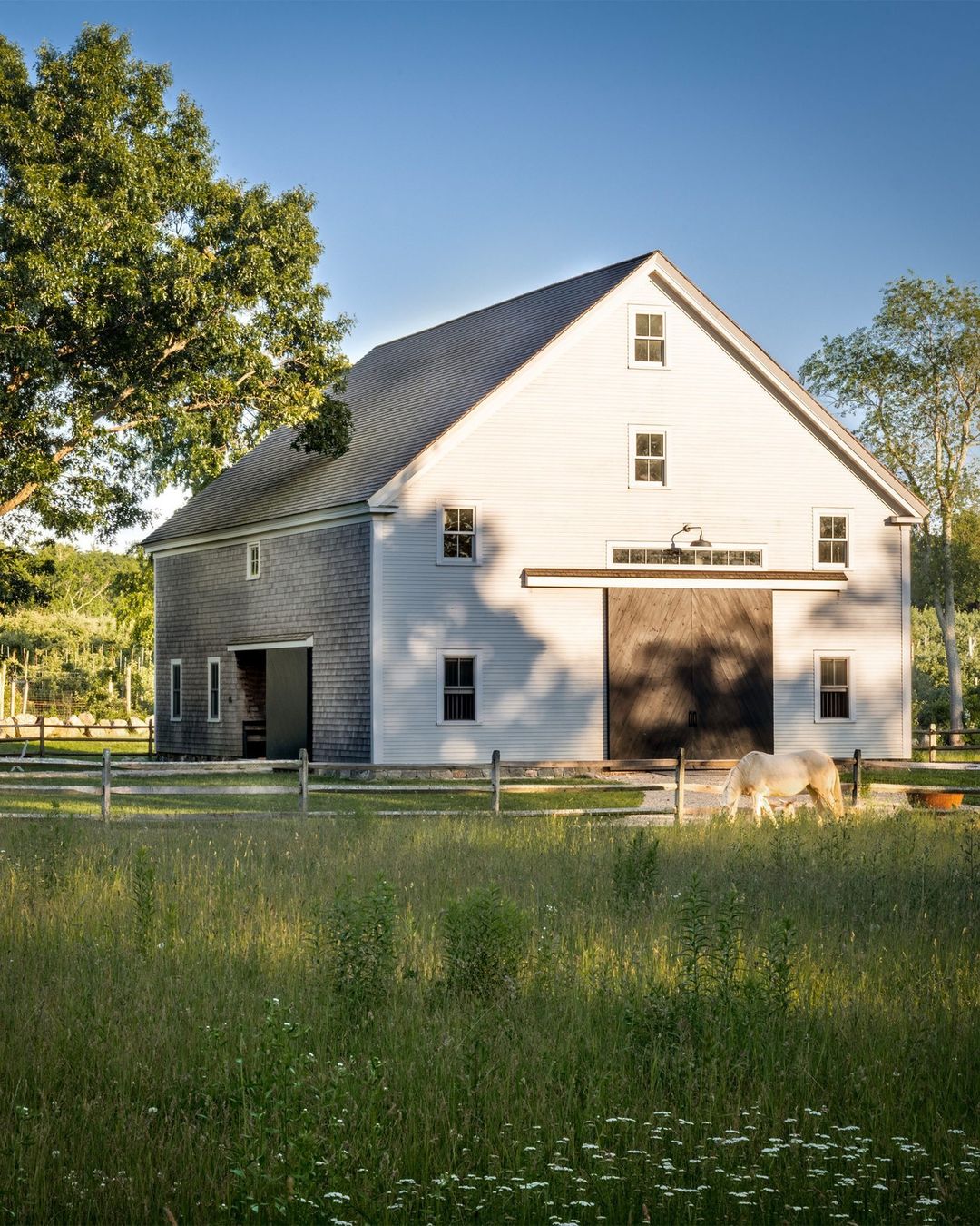 A serene farmstead with a large white barn and a grazing horse