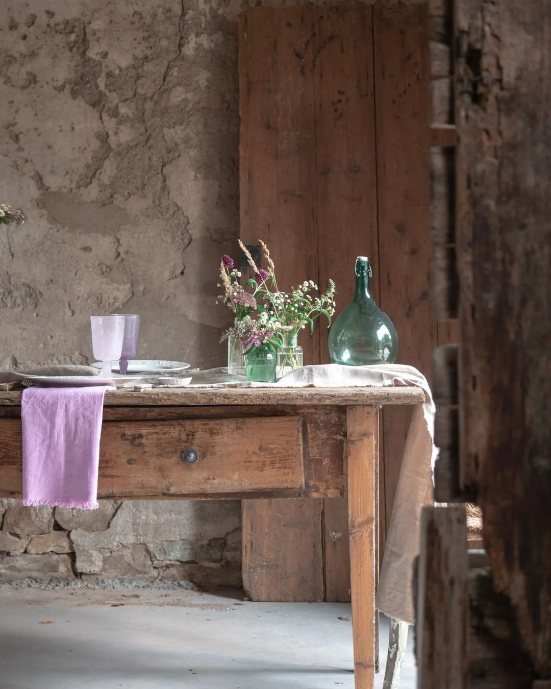 A rustic and serene dining corner featuring an aged wooden table with a lavender-hued napkin