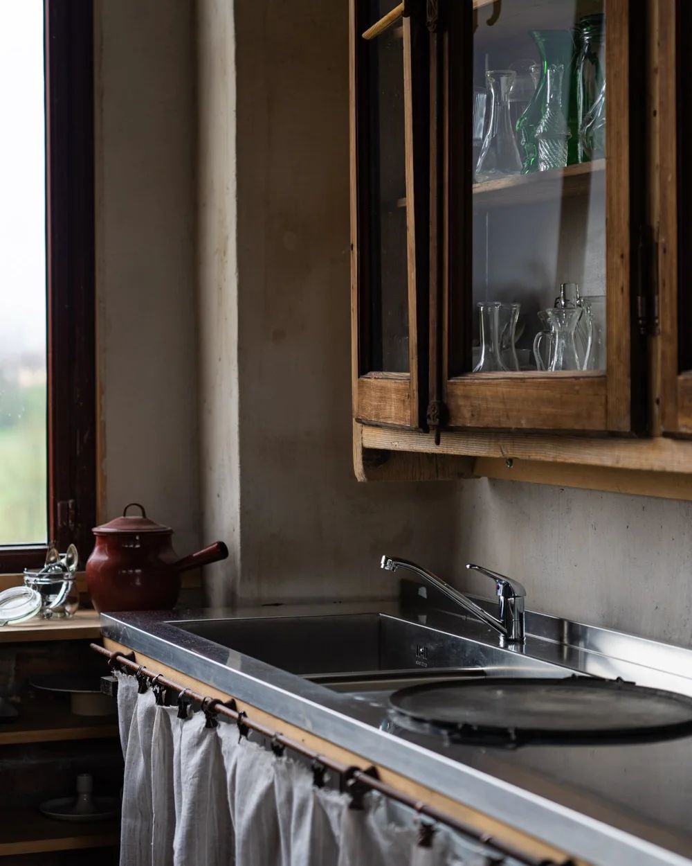 A rustic kitchen setting featuring an undermount sink, with a red enamel kettle on the counter