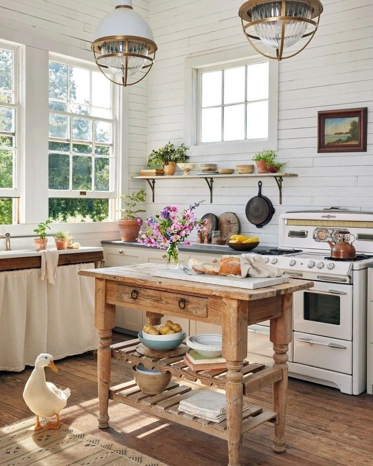 A rustic and charming kitchen featuring a vintage island table, open shelving, and a visiting duck on the floor.