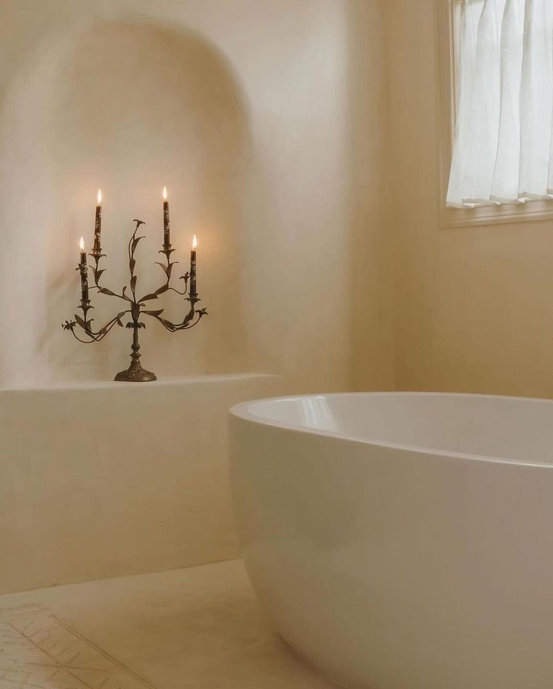 A serene bathroom with smooth contours featuring a free-standing tub and a candelabra.