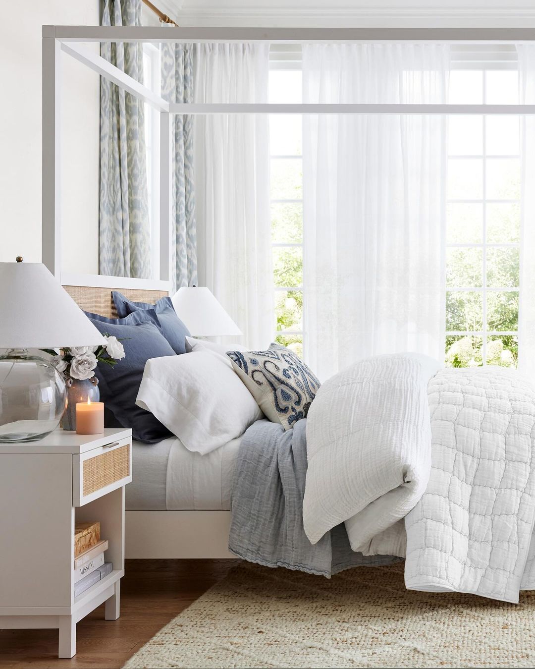 A serene and well-appointed bedroom featuring a white four-poster bed with plush blue and gray bedding