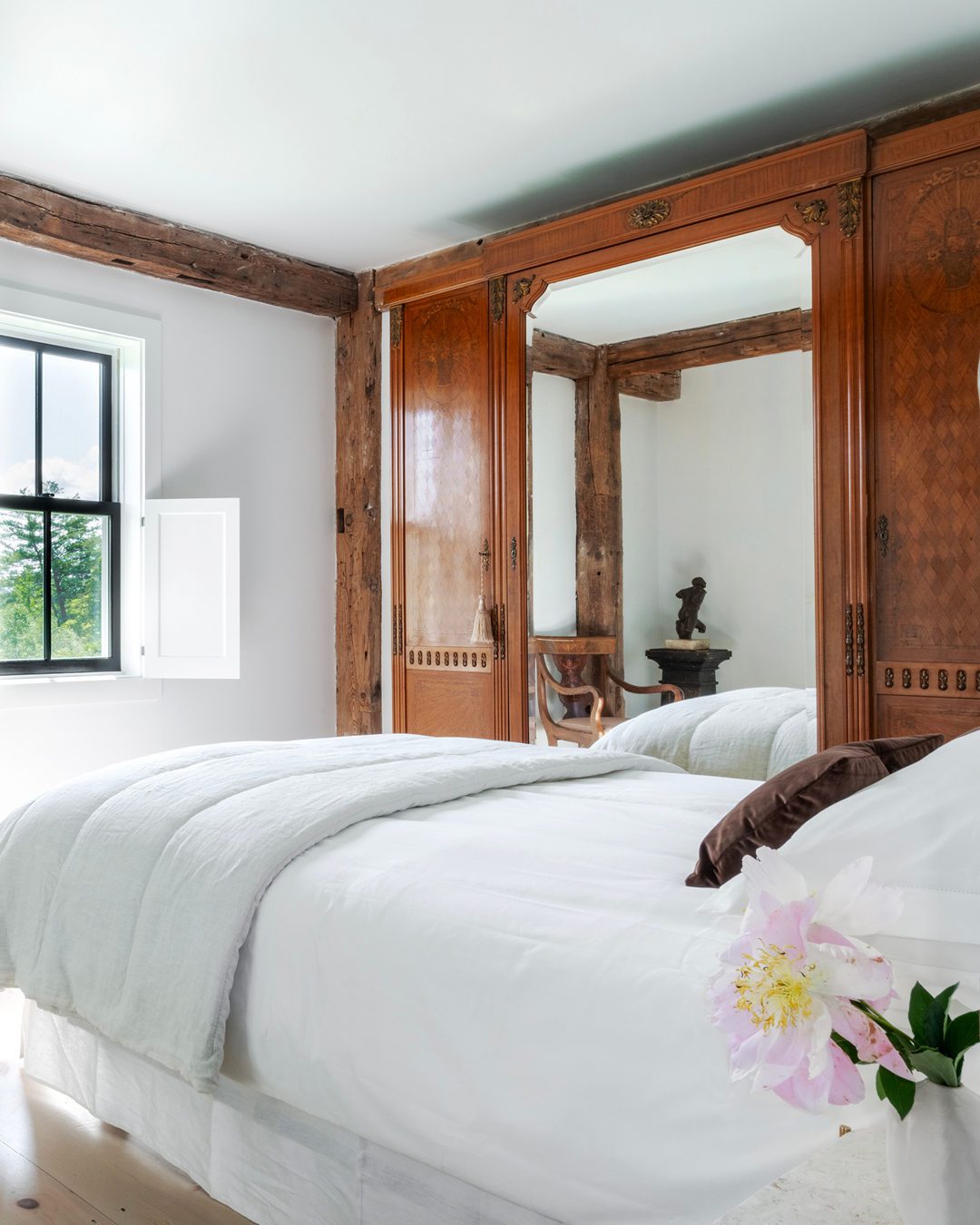 A serene bedroom featuring an ornate wooden mirror reflecting a simply adorned bed