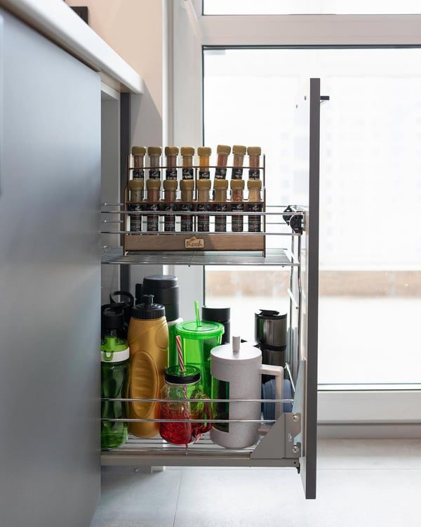 A neatly organized pull-out kitchen cabinet with labelled spice jars on top and assorted bottles and utensils below