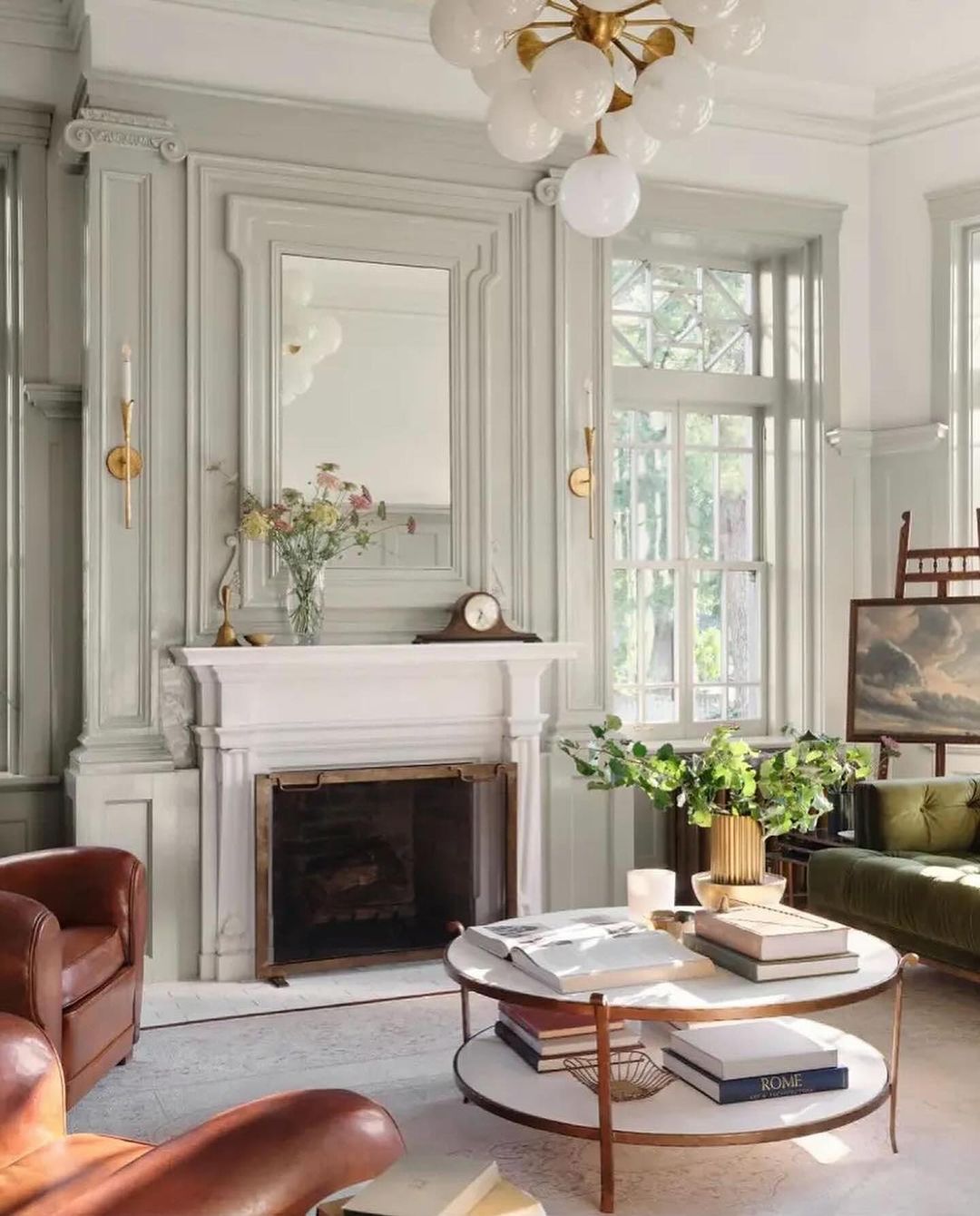 A classic living room setup with natural light illuminating the carved wooden fireplace, leather furniture, and brass accents.