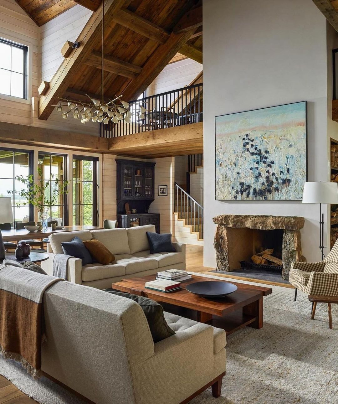 A warm and inviting living room designed with exposed wooden beams, a large stone fireplace, and a combination of cozy textiles and seating arrangements.