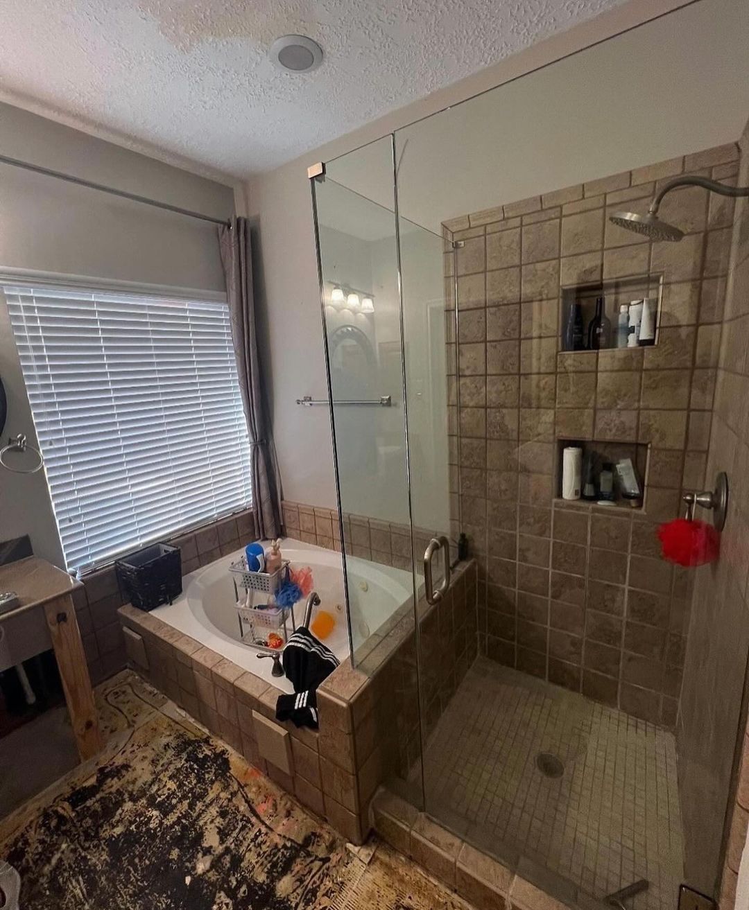 A spacious bathroom featuring a tiled tub, glass-walled shower, and scattered bath toys