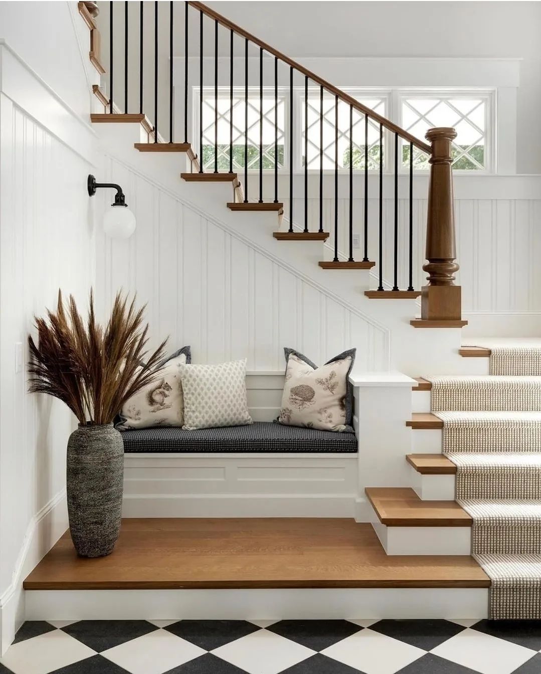 A chic and cozy stairwell featuring a built-in bench and bold black and white checkered flooring.