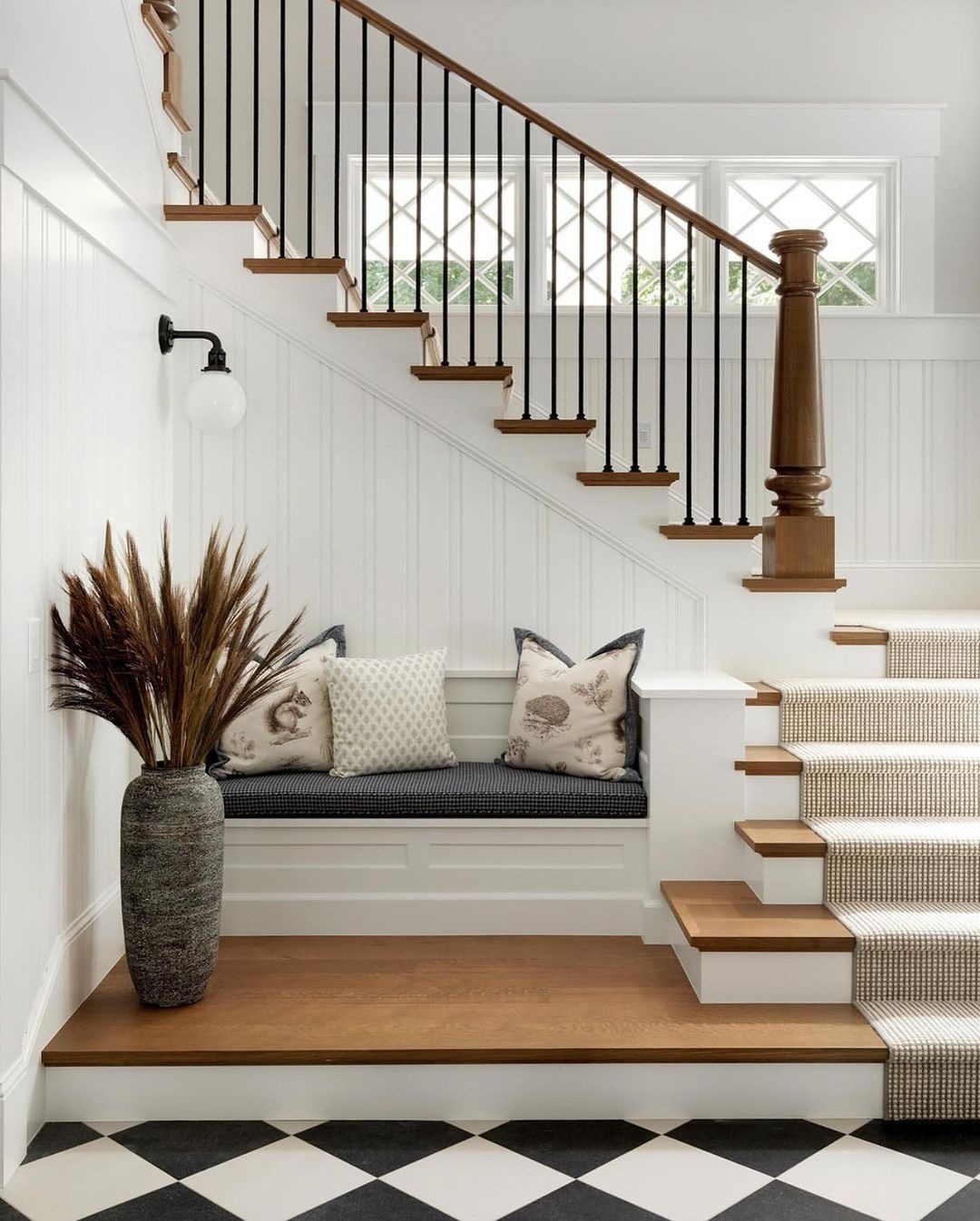 A chic and welcoming entryway featuring a black and white checkered floor, a built-in bench, and a staircase with wood accents