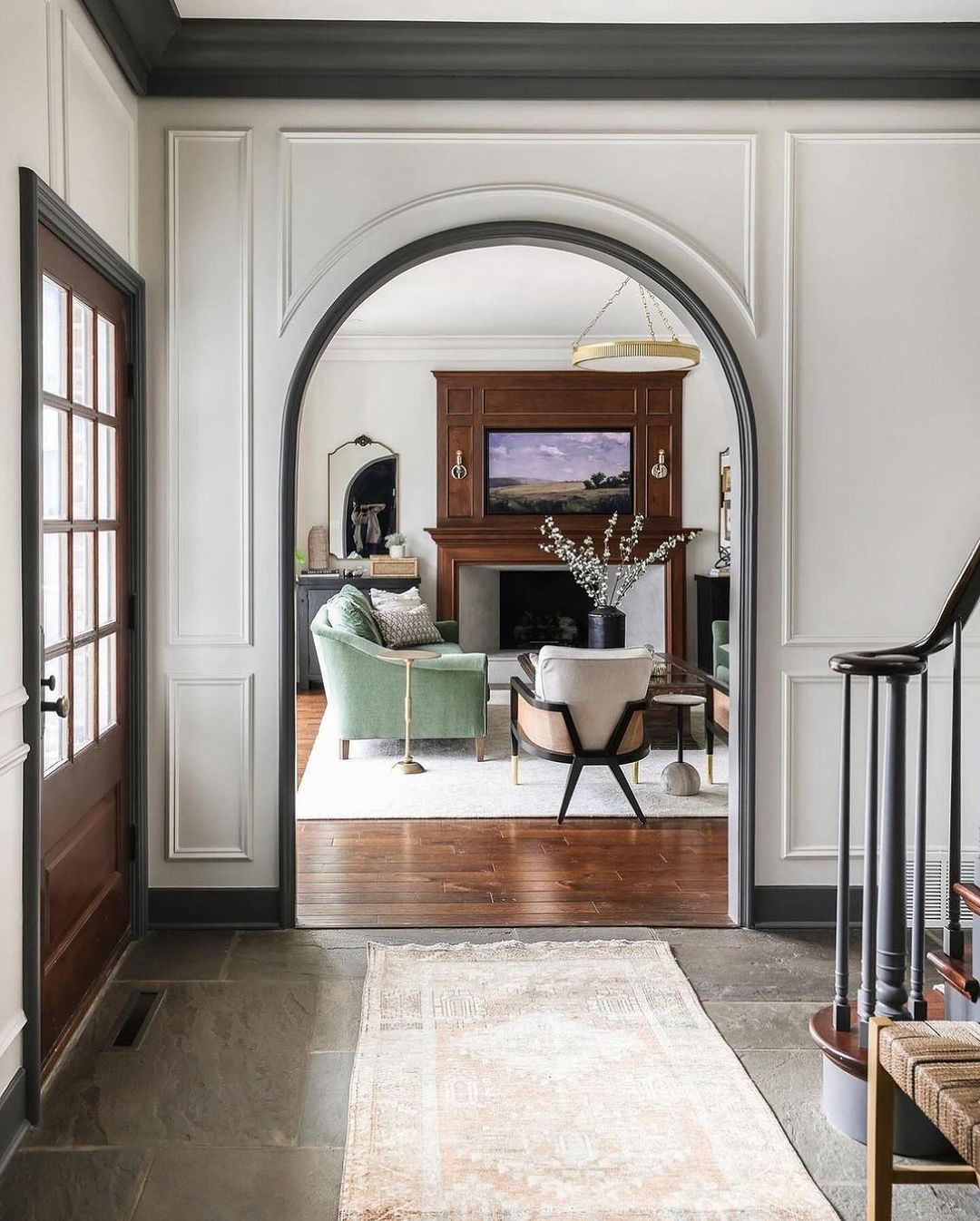 A harmoniously designed archway in a traditional-style home with contrasting dark wood floors leading into a cozy living space featuring a classic fireplace and tastefully appointed furnishings.