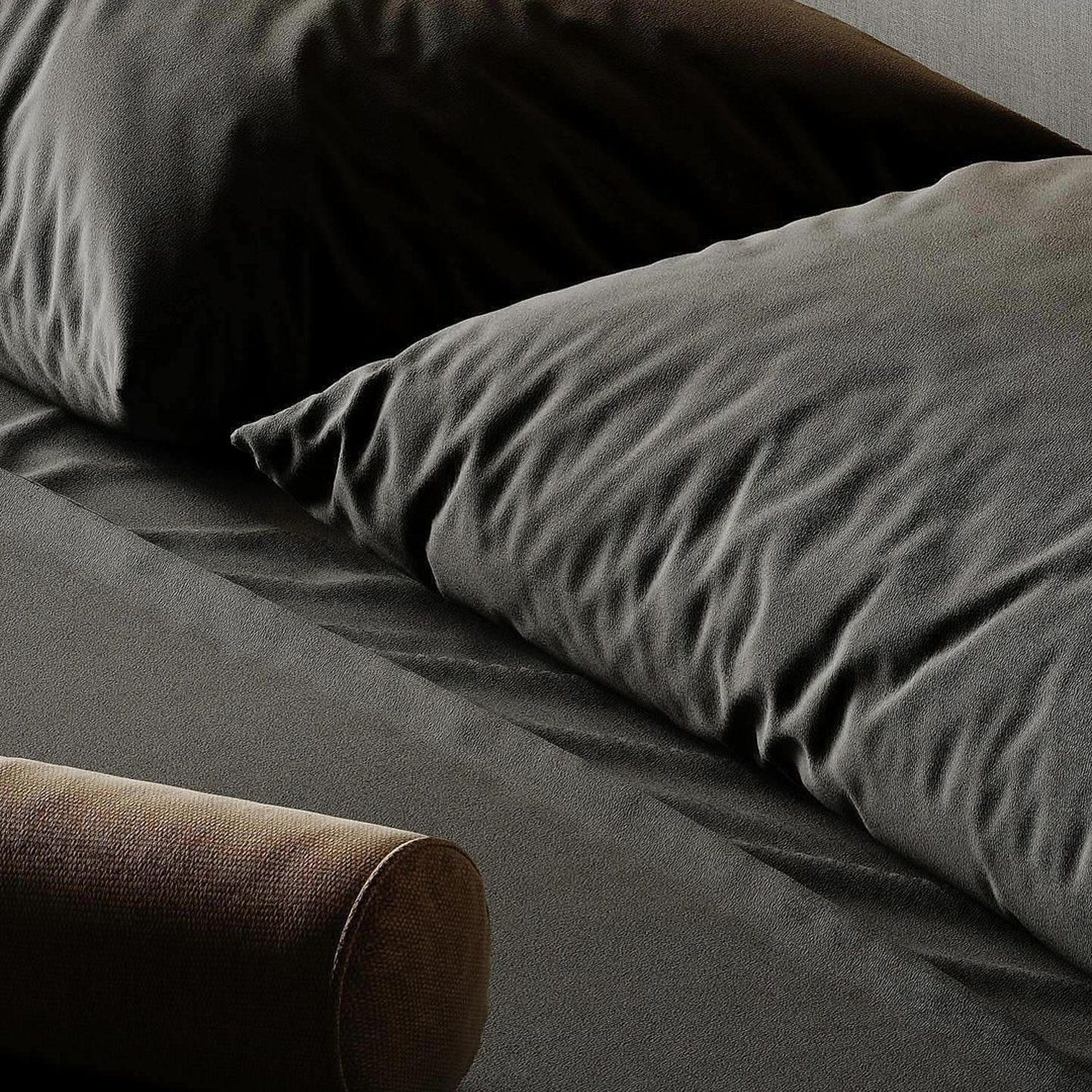 A neatly made bed with luxurious dark grey bedding and an earth-toned bolster pillow