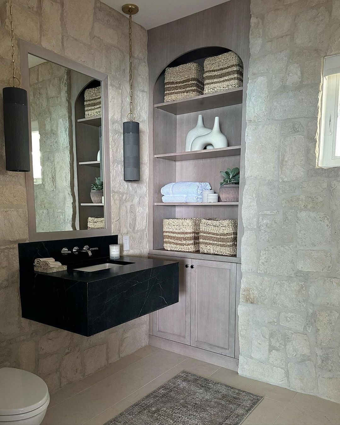 A stylish bathroom combining textured natural stone walls with a sleek black basin