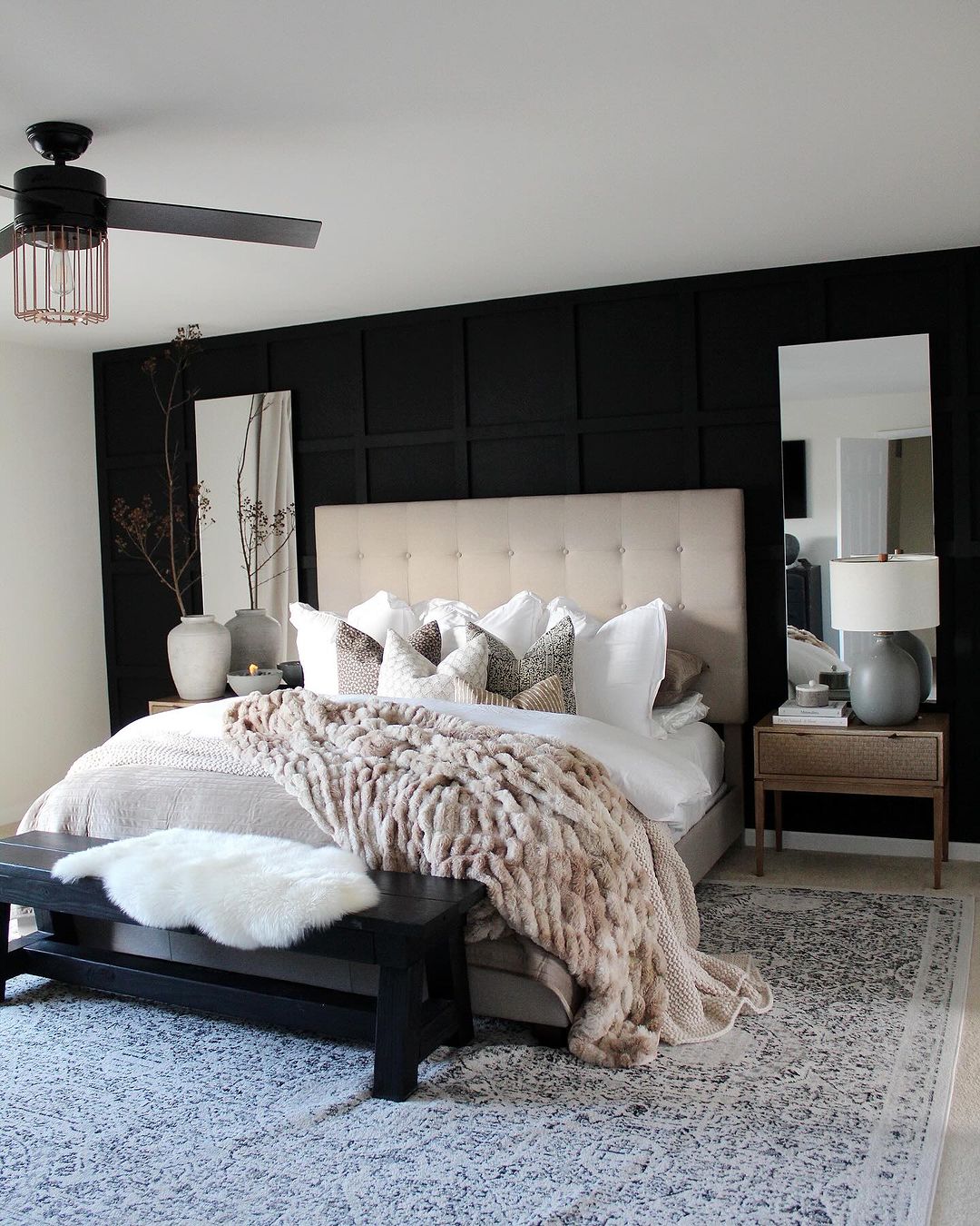 A tastefully designed bedroom with a bold black accent wall and a plush tufted headboard