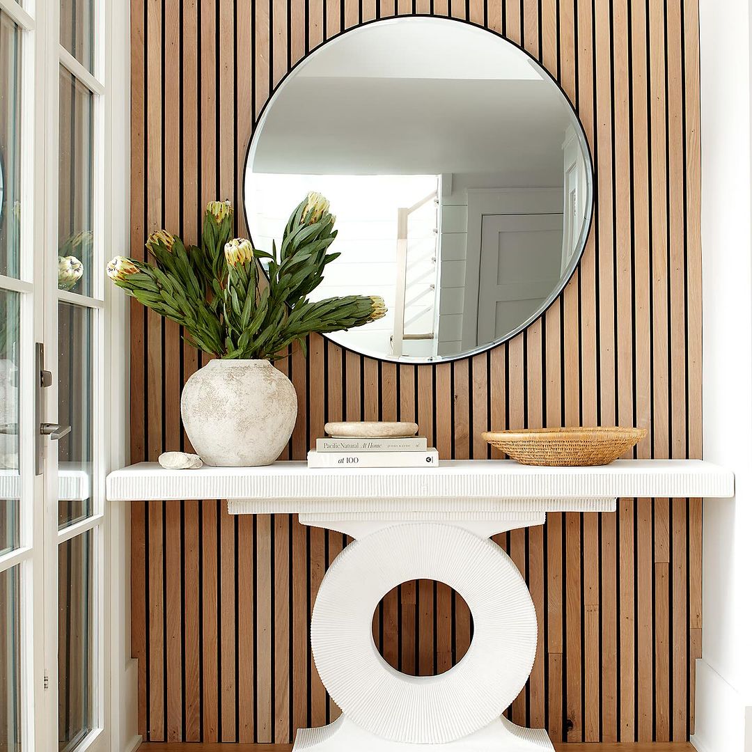 A modern entryway featuring a circular mirror against a warm wooden slat background