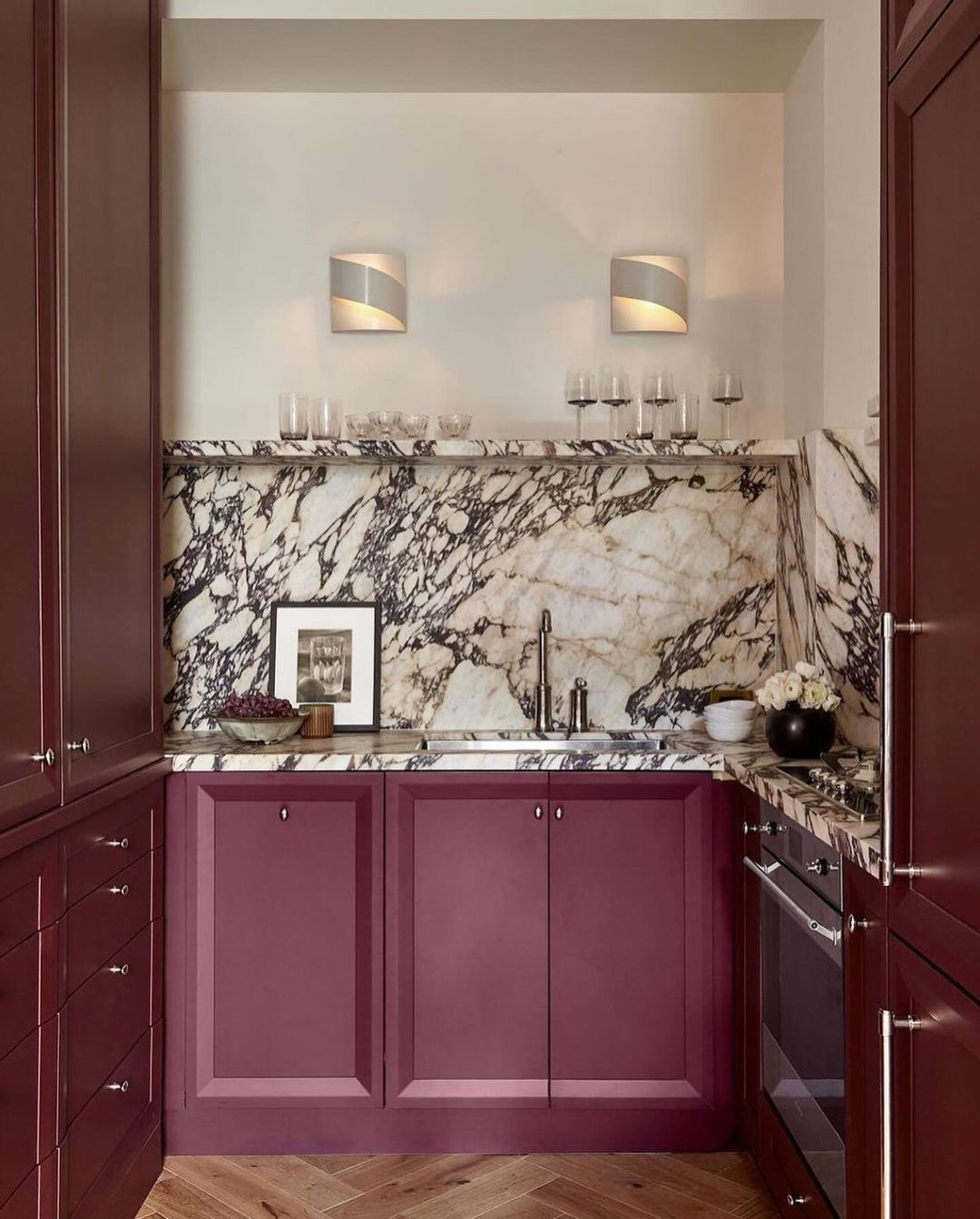 A chic bar nook with deep maroon cabinetry and a striking marble backsplash