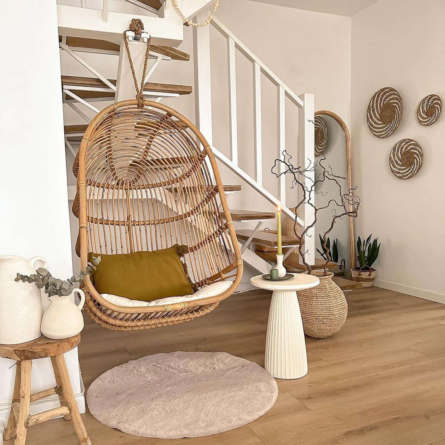 A cozy corner featuring a rattan hanging chair with a plush olive cushion