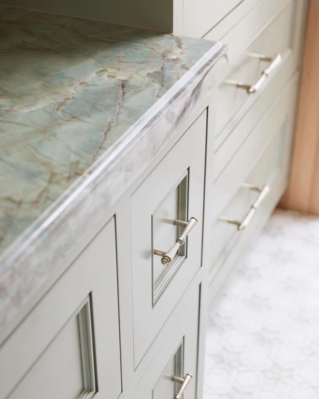 A detailed view of a kitchen cabinet featuring marble countertop and modern pull handles