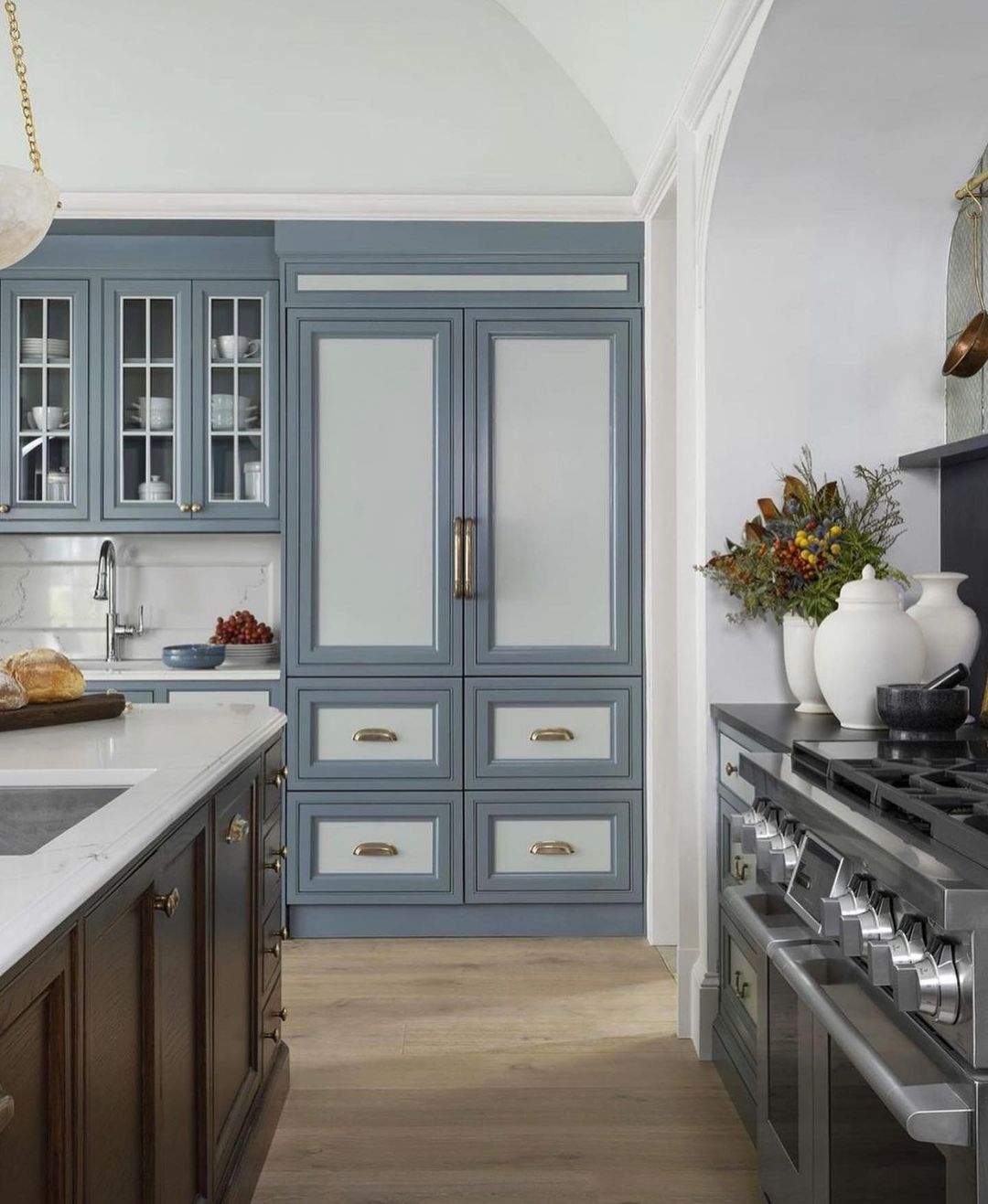 A chic blue-toned kitchen featuring brass hardware and a professional stove