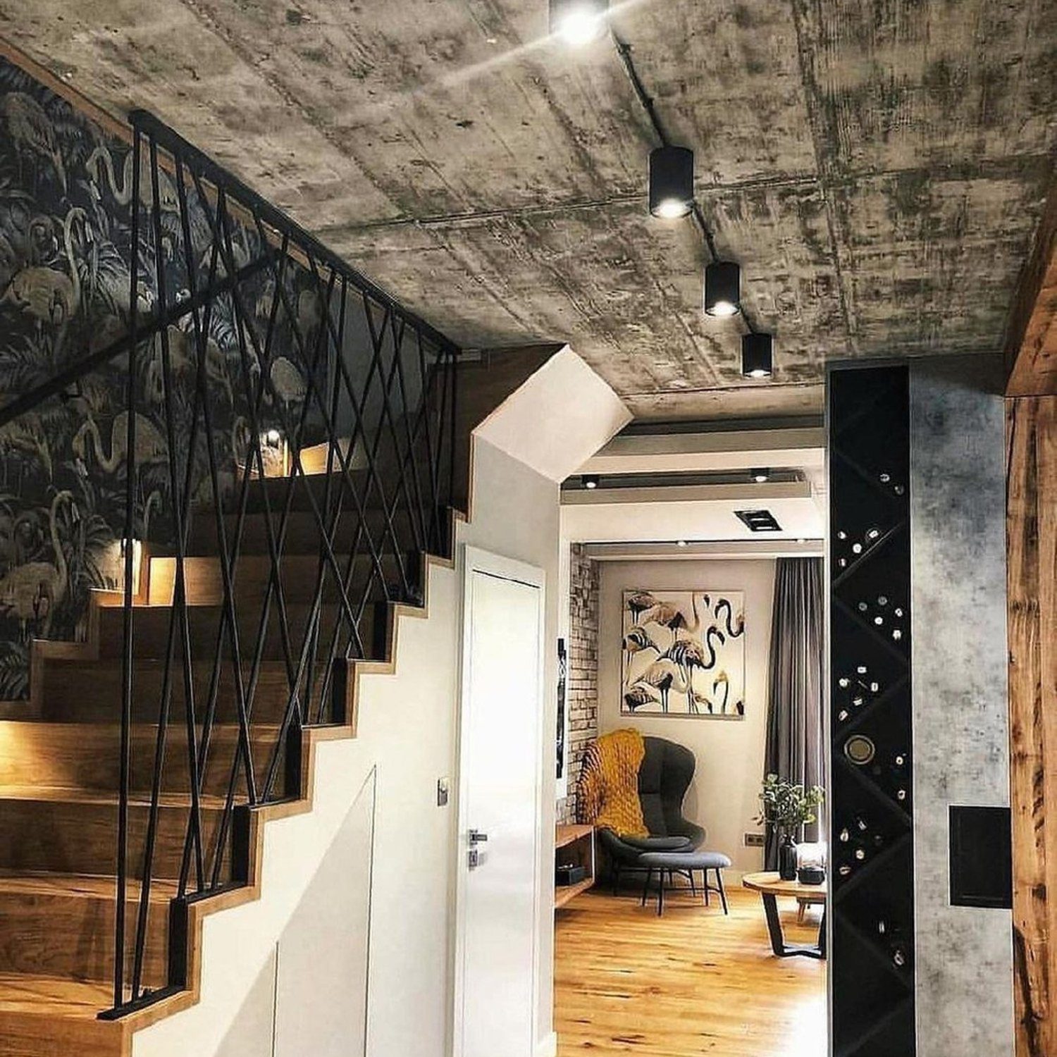 A stylish interior with a blend of modern and rustic elements, featuring exposed concrete ceiling, open wooden staircase, and a cozy seating area with wall art.