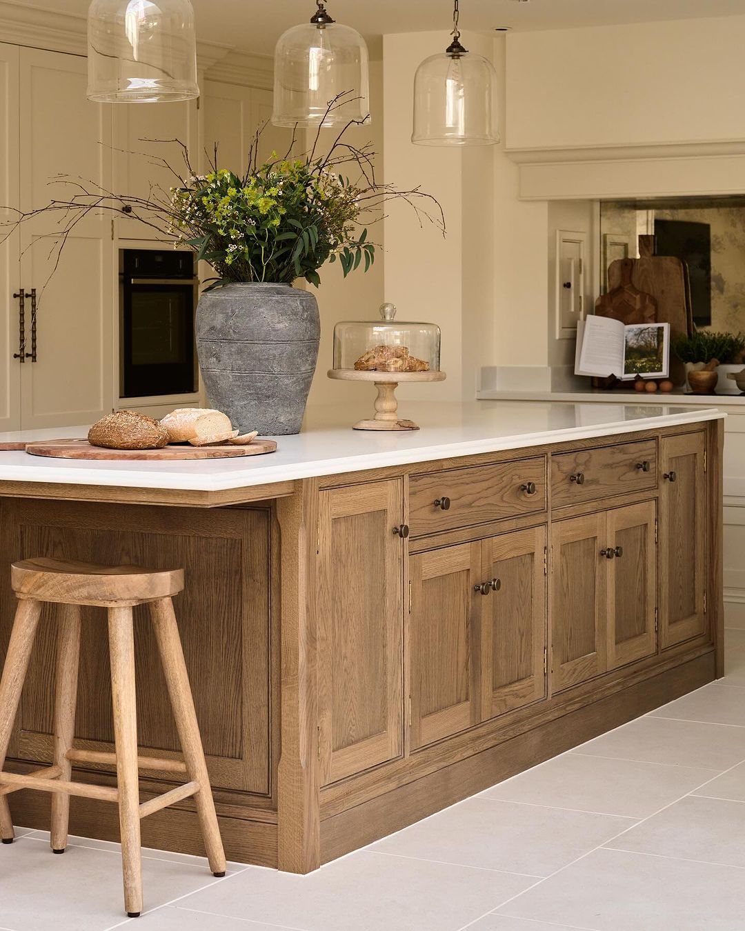 A tastefully designed kitchen featuring a rustic wooden island with a white countertop, adorned with a large vase of wildflowers and artisan breads