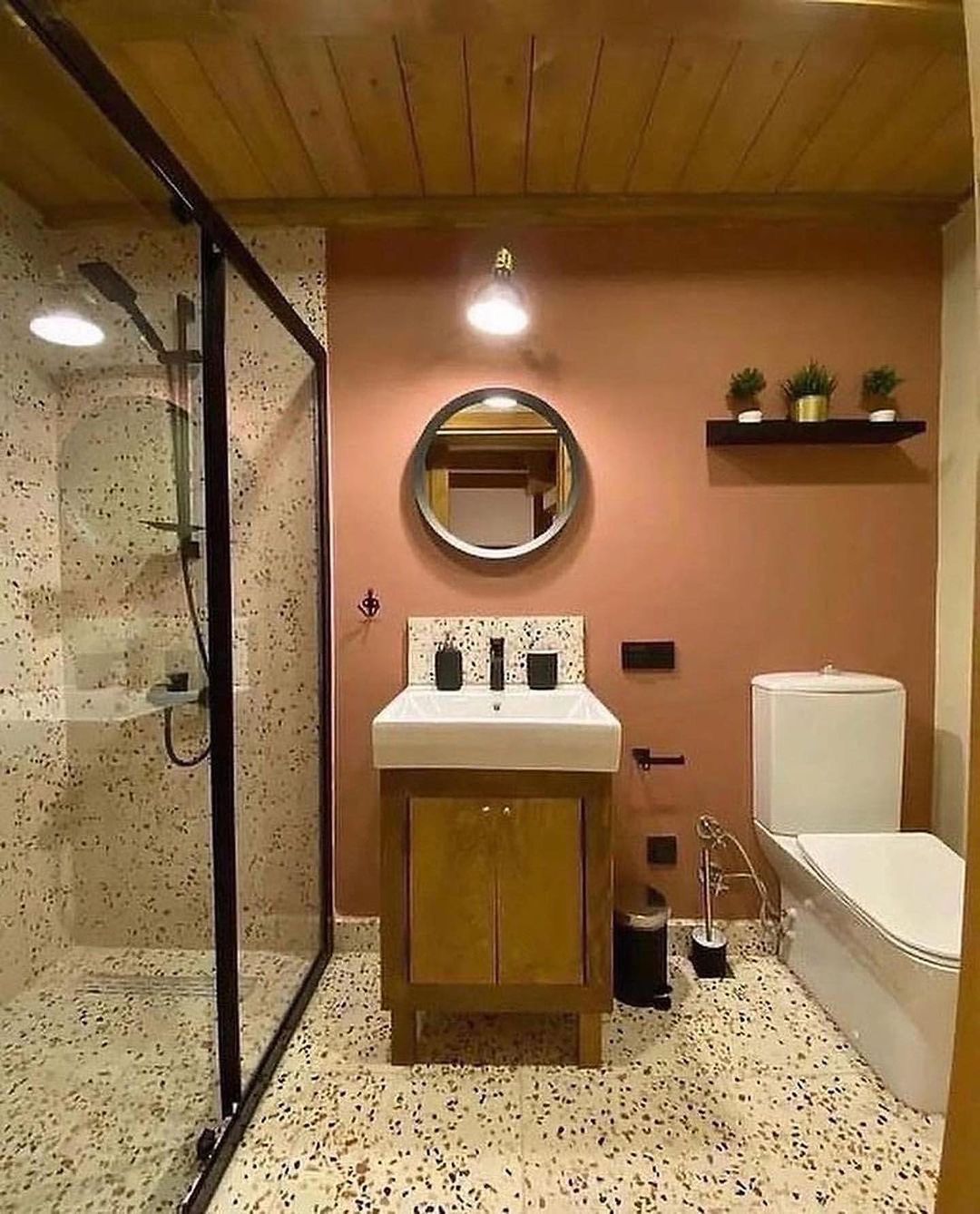 A modern terrazzo floored bathroom featuring a wall-mounted terrazzo sink, a glass walk-in shower, and a wooden ceiling.