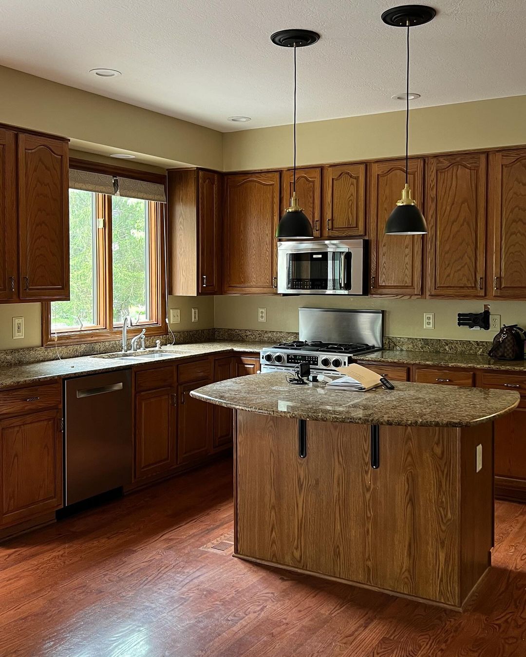 A warm and inviting kitchen featuring classic wood cabinetry, granite countertops, and modern hanging pendant lights.