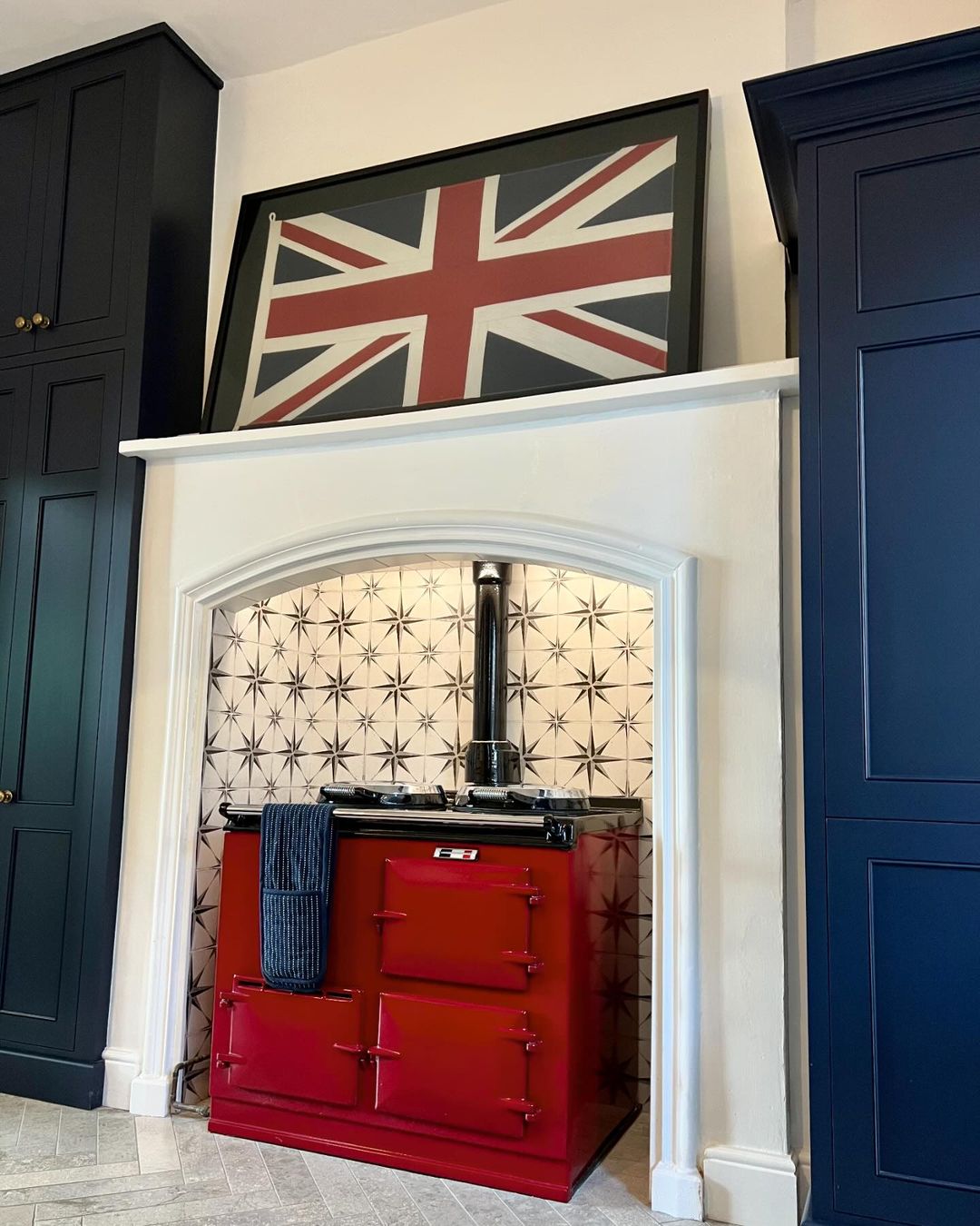 A vibrant kitchen featuring a bold red AGA cooker set against a patterned tile backsplash, flanked by deep blue cabinetry