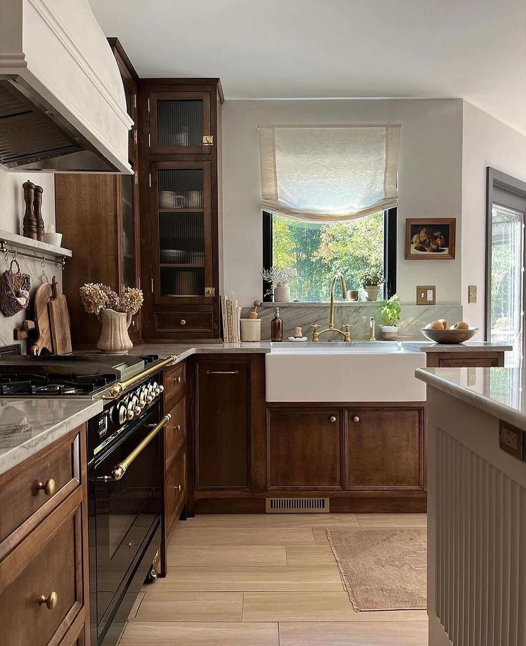 A warm and inviting kitchen featuring rich dark wood cabinets, brass hardware, a classic white farmhouse sink, and a vintage-inspired stove