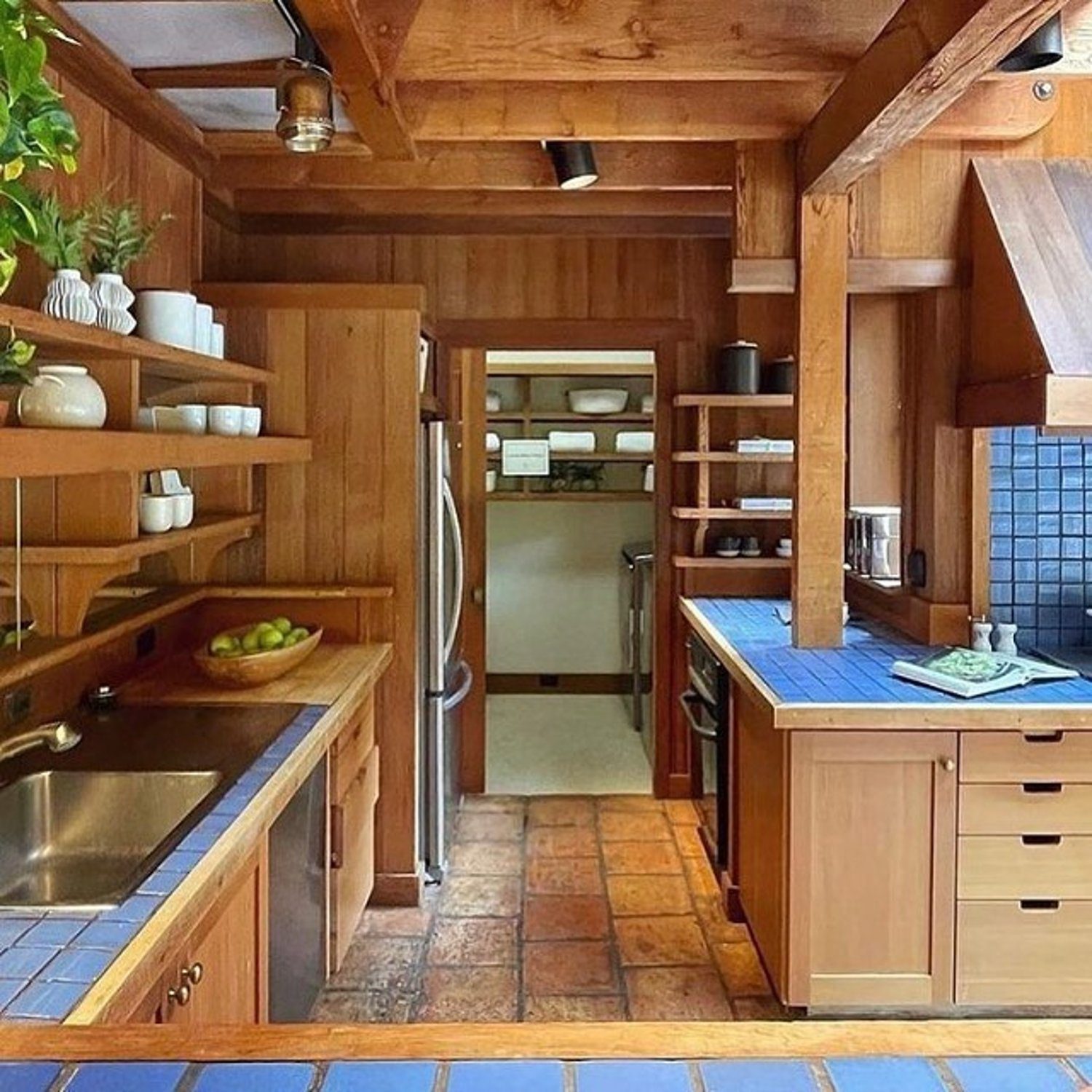 A cozy and traditional kitchen featuring rich wooden cabinetry, terracotta floor tiles, and blue-tiled countertops