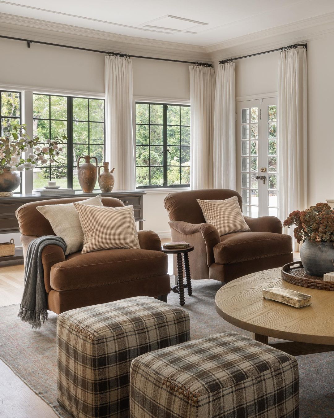 A cozy traditional living room design featuring plush brown armchairs, matching plaid ottomans, and a round wooden coffee table