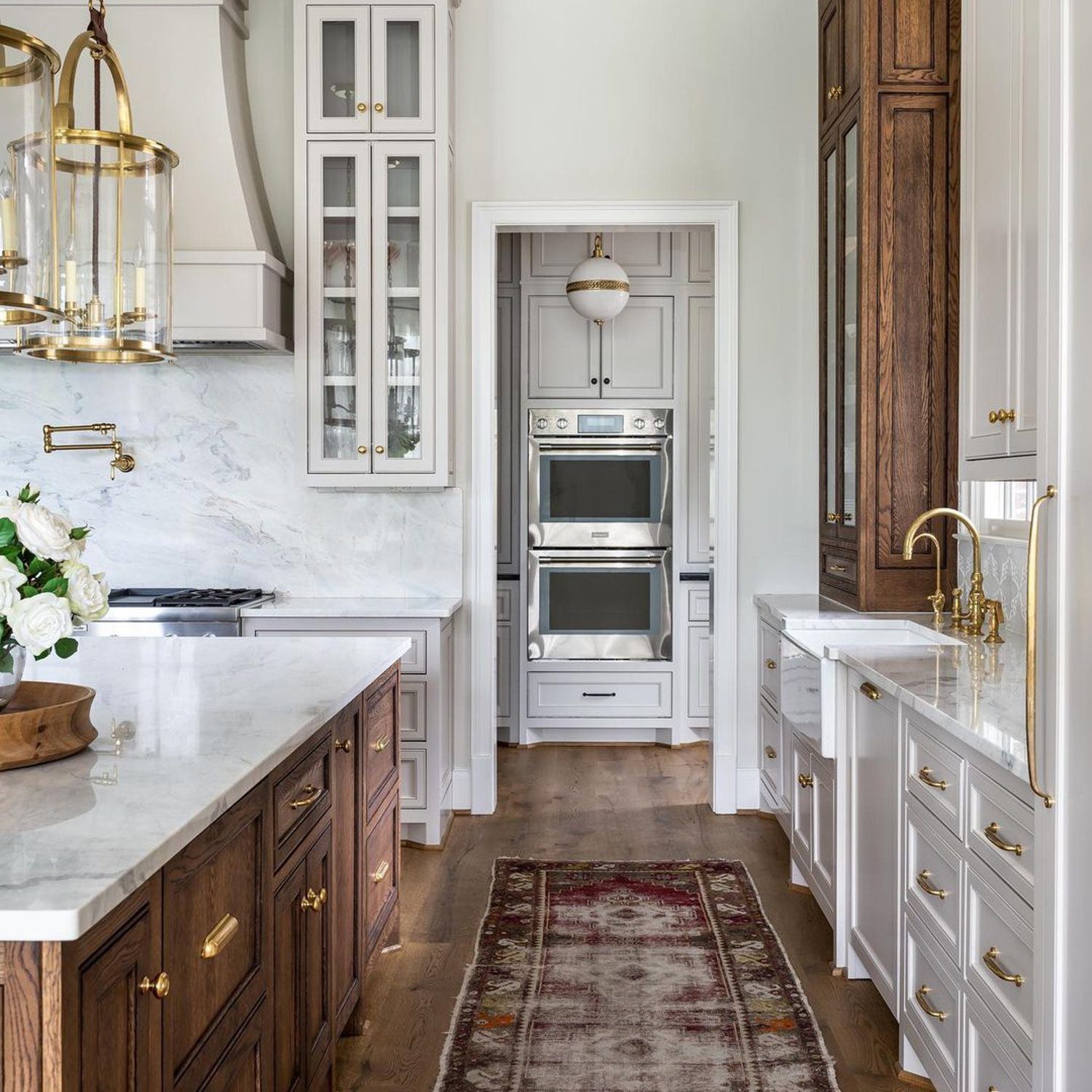 Elegant transitional kitchen design featuring a mix of dark wood and white cabinetry, marble countertops, a brass pendant light, and a vintage-style runner