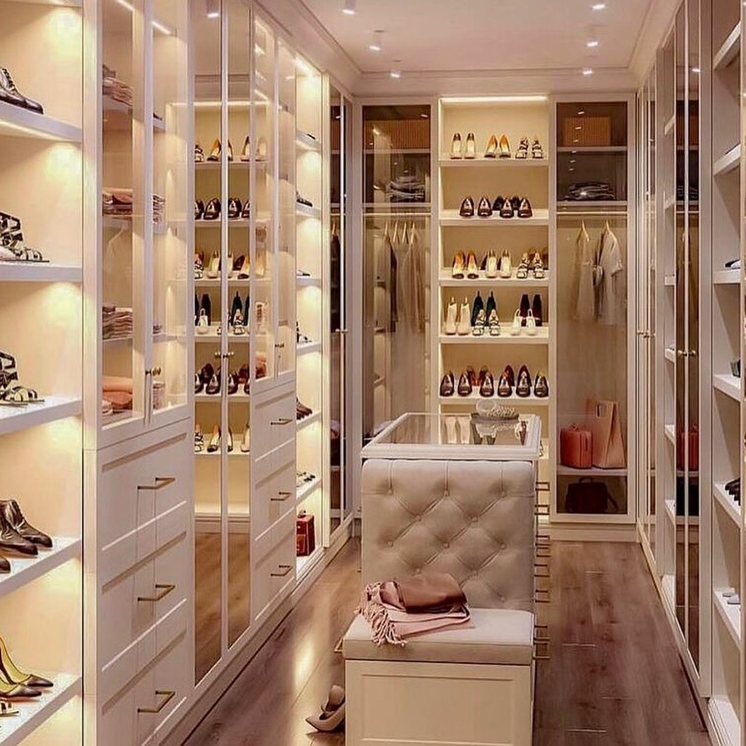 Elegant walk-in closet featuring ample shoe storage, a plush seating area, and warm accent lighting.