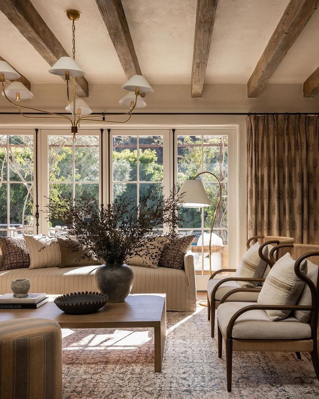 A cozy and inviting living room with exposed wooden beams, ample natural light, and comfortable furnishings