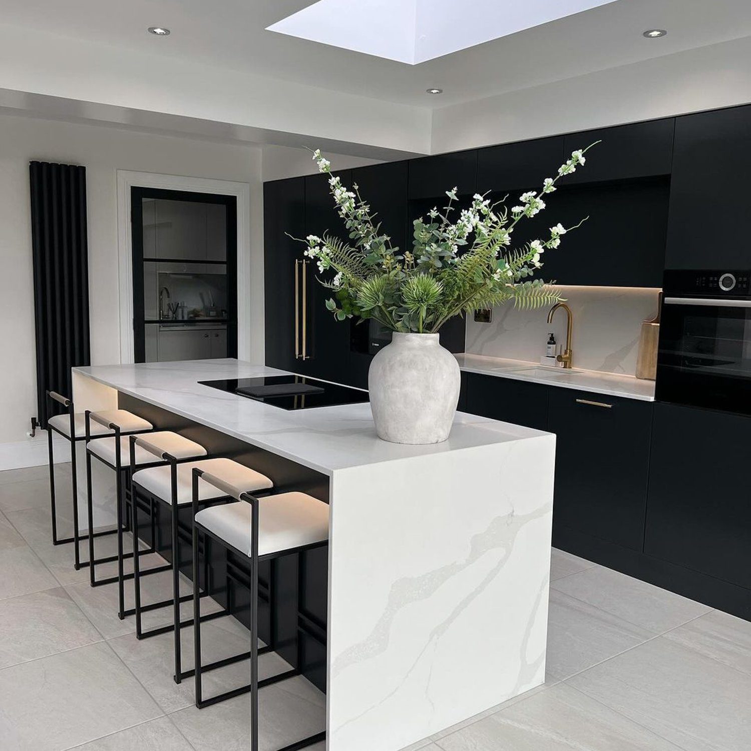 A sleek and contemporary kitchen featuring matte black cabinetry, a white marble island with bar seating, and modern appliances