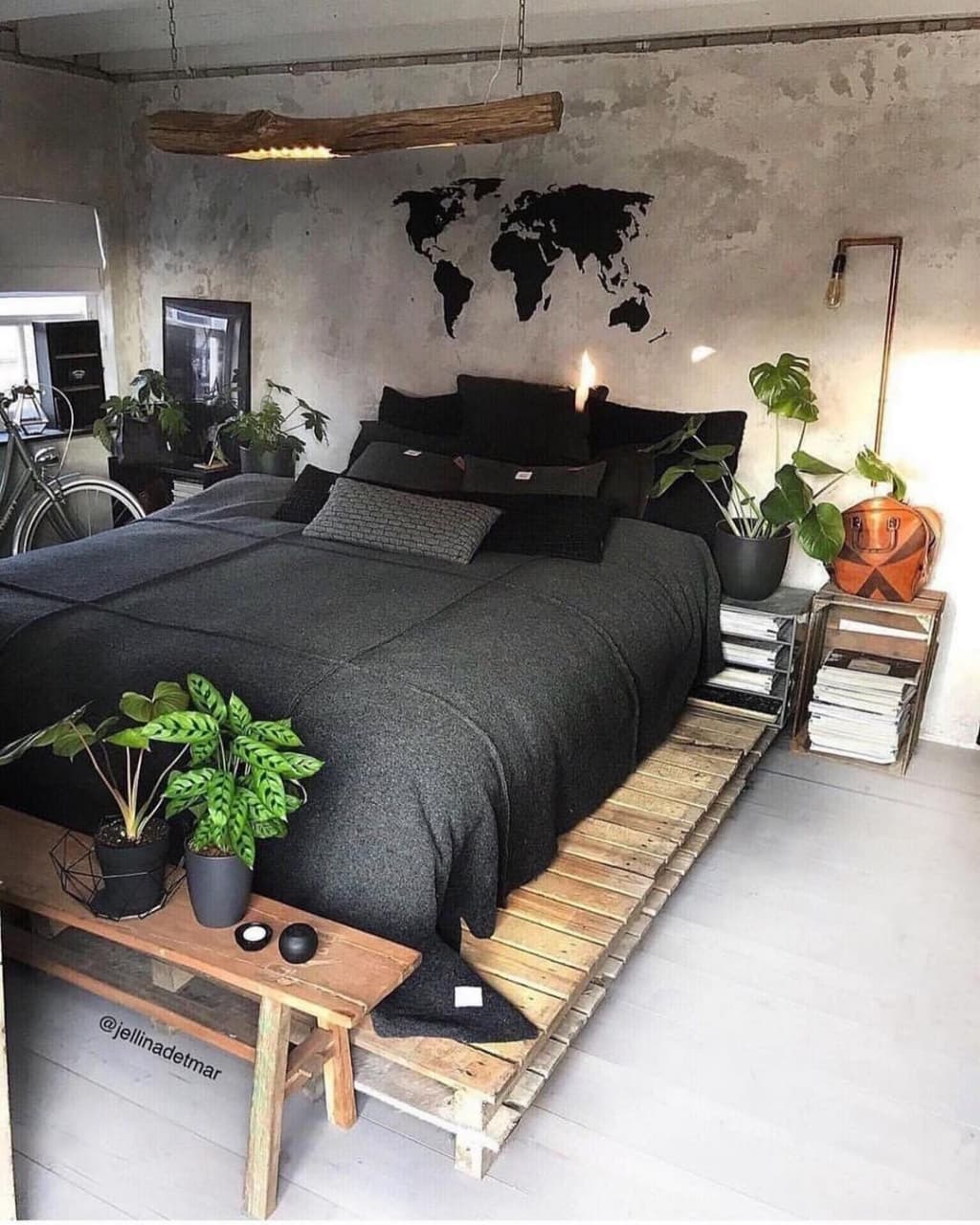 A minimalist industrial bedroom featuring a world map mural above a low-lying bed constructed from pallets